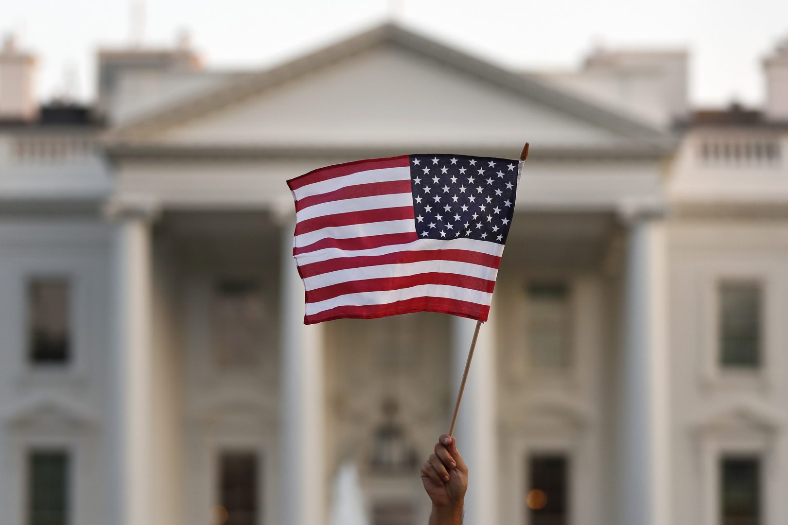 FILE - In this Sept. 5, 2017, file photo, a flag is waved outside the White House, in Washington. The Trump administration is extending a ban on green cards issued outside the United States until the end of 202 and adding many temporary work visas to the freeze, including those used heavily by technology companies and multinational corporations. 