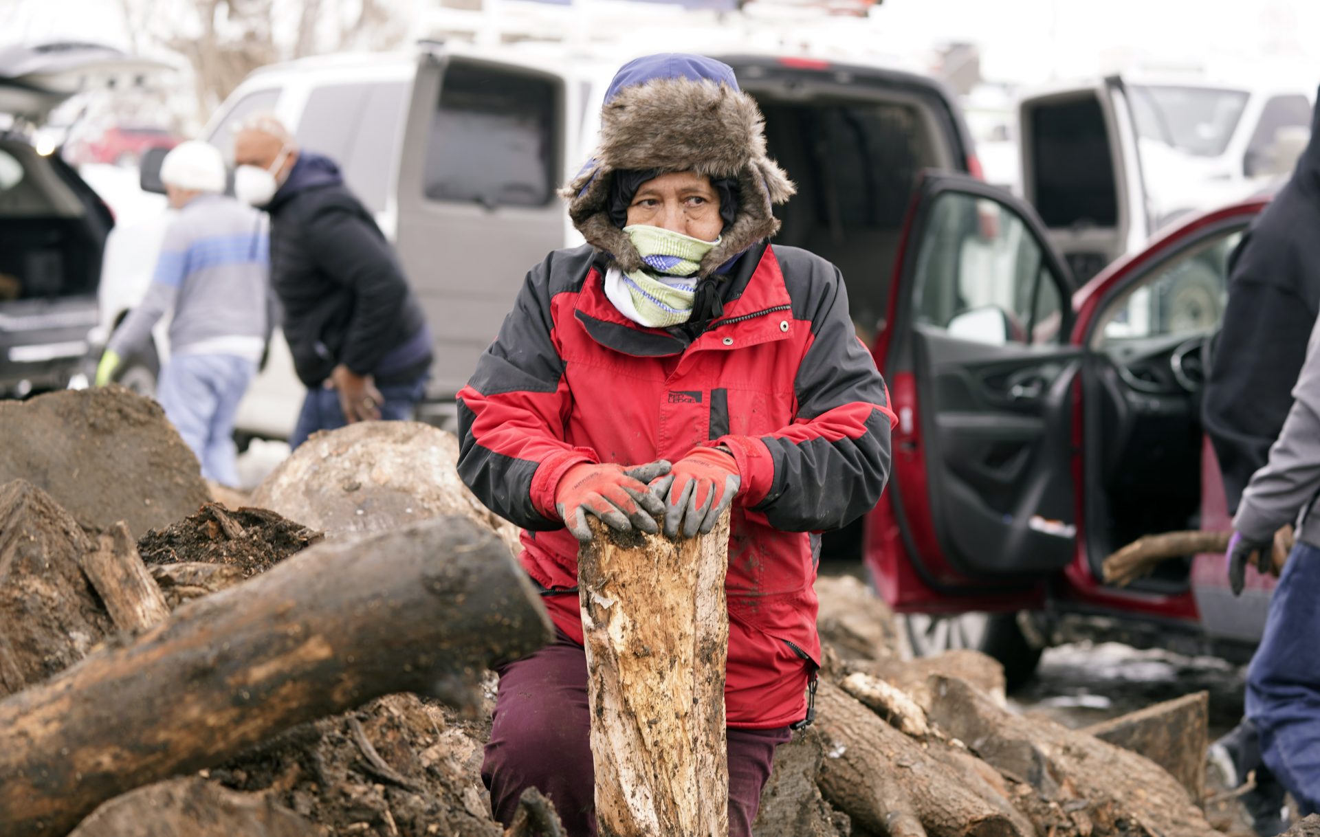 Rufina Moya helps collect firewood to burn for warmth from wood heap opened to the public Wednesday, Feb. 17, 2021, in Dallas. With a long line of folks waiting in their vehicles, groups of thirteen were allowed six minutes to load as much wood as they could carry away from the recycling center that started selling firewood.