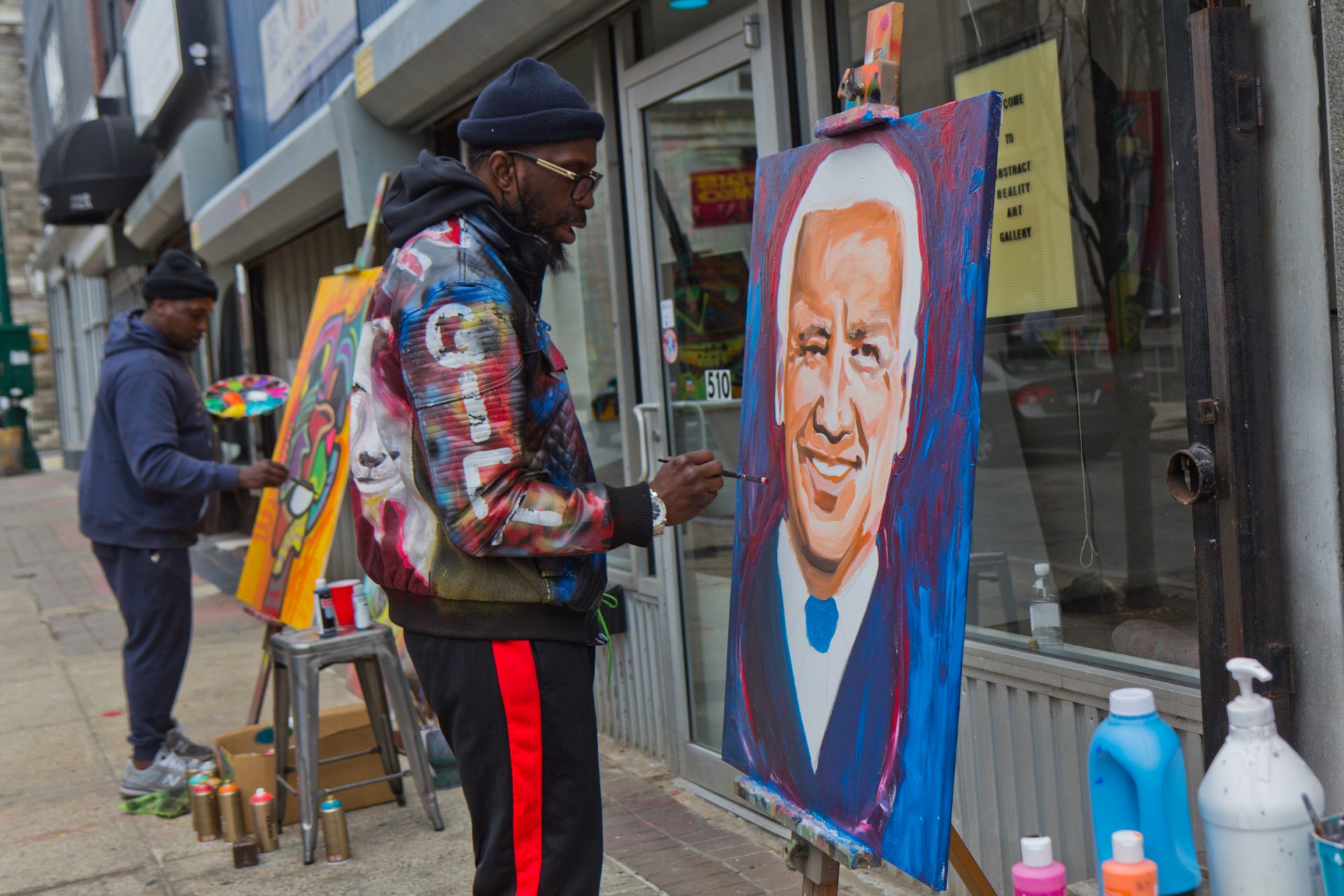 Emmanuel Fitzpatrick (right) paints President Biden in front of Abstract Reality Art Gallery in Chester, Pa., on March 16, 2021.