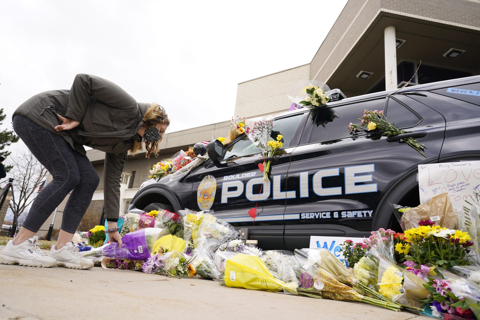A woman leaves a bouquet of flowers next to a police cruiser parked outside the Boulder Police Department after an officer was one of the victims of a mass shooting at a King Soopers grocery store Tuesday, March 23, 2021, in Boulder, Colo.
