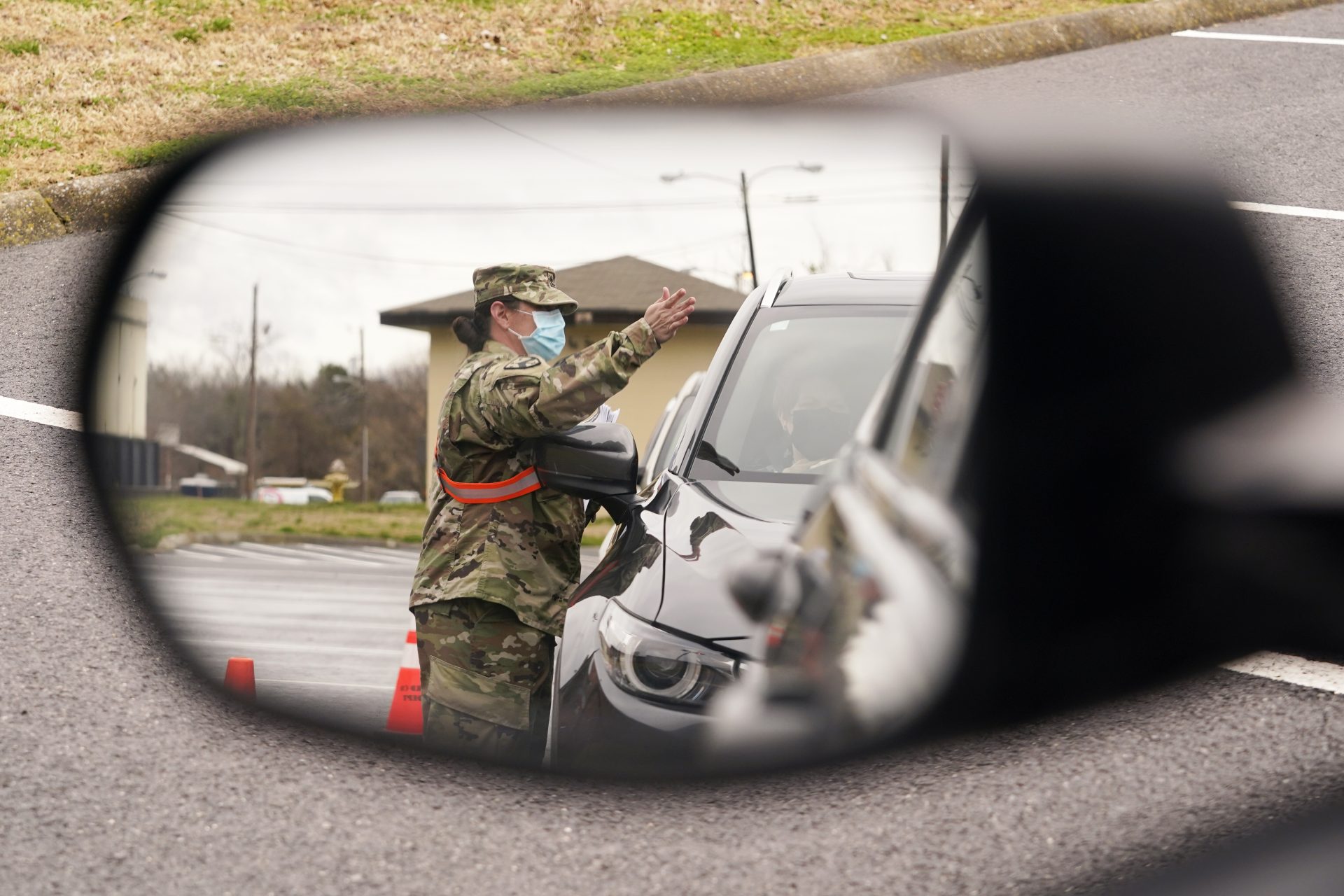 A National Guard soldier directing drivers is reflected in the mirror of a car waiting in a COVID-19 vaccination line Feb. 26, 2021, in Shelbyville, Tenn.