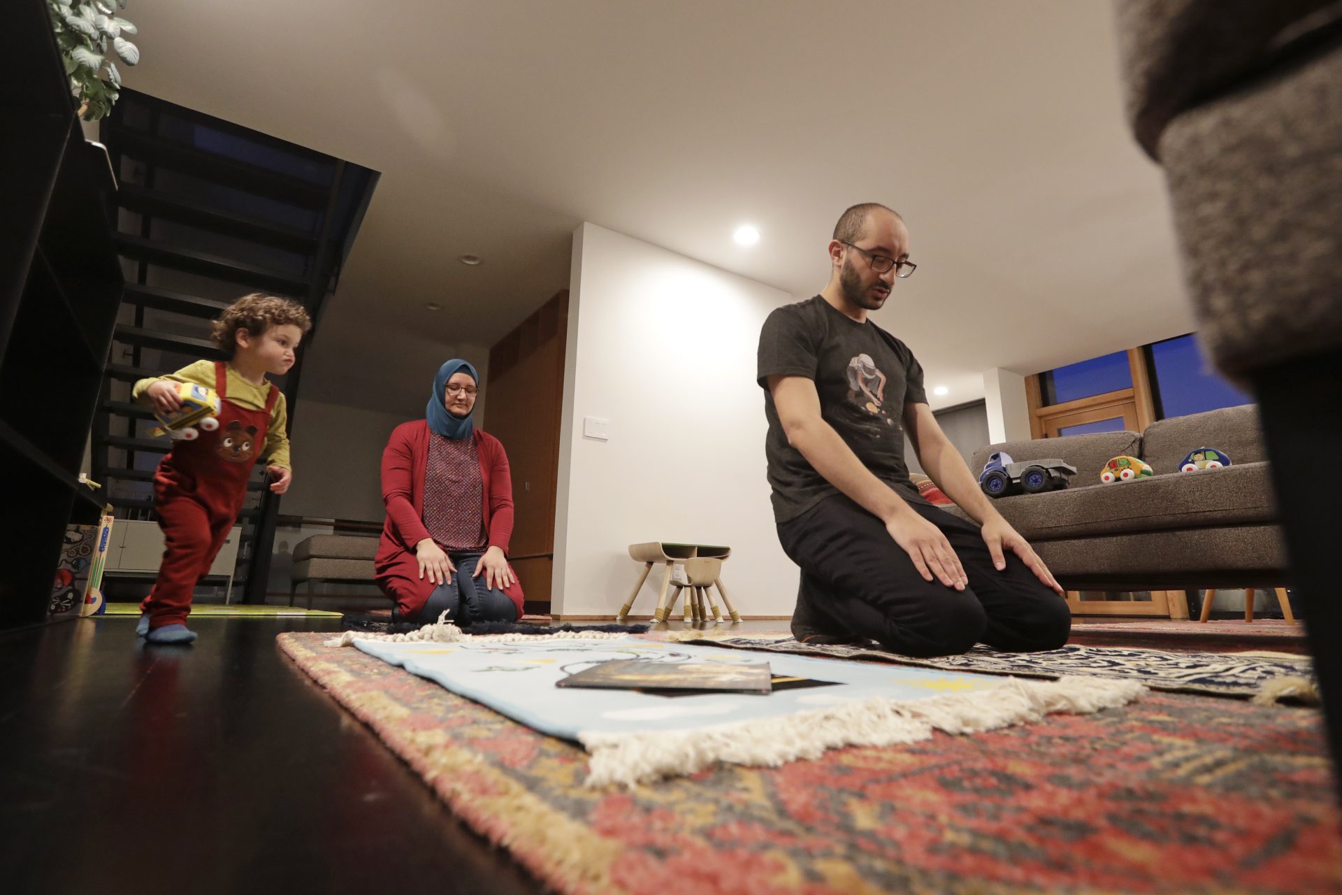 In this Tuesday, April 28, 2020 file photo, Ahmad Kamel, right, performs the Maghrib prayer with his wife, Nadia Chaouch, as their son Ahmad Kamel runs past after the family broke the Ramadan daily fast just after sunset in their home, during the coronavirus outbreak in Seattle.