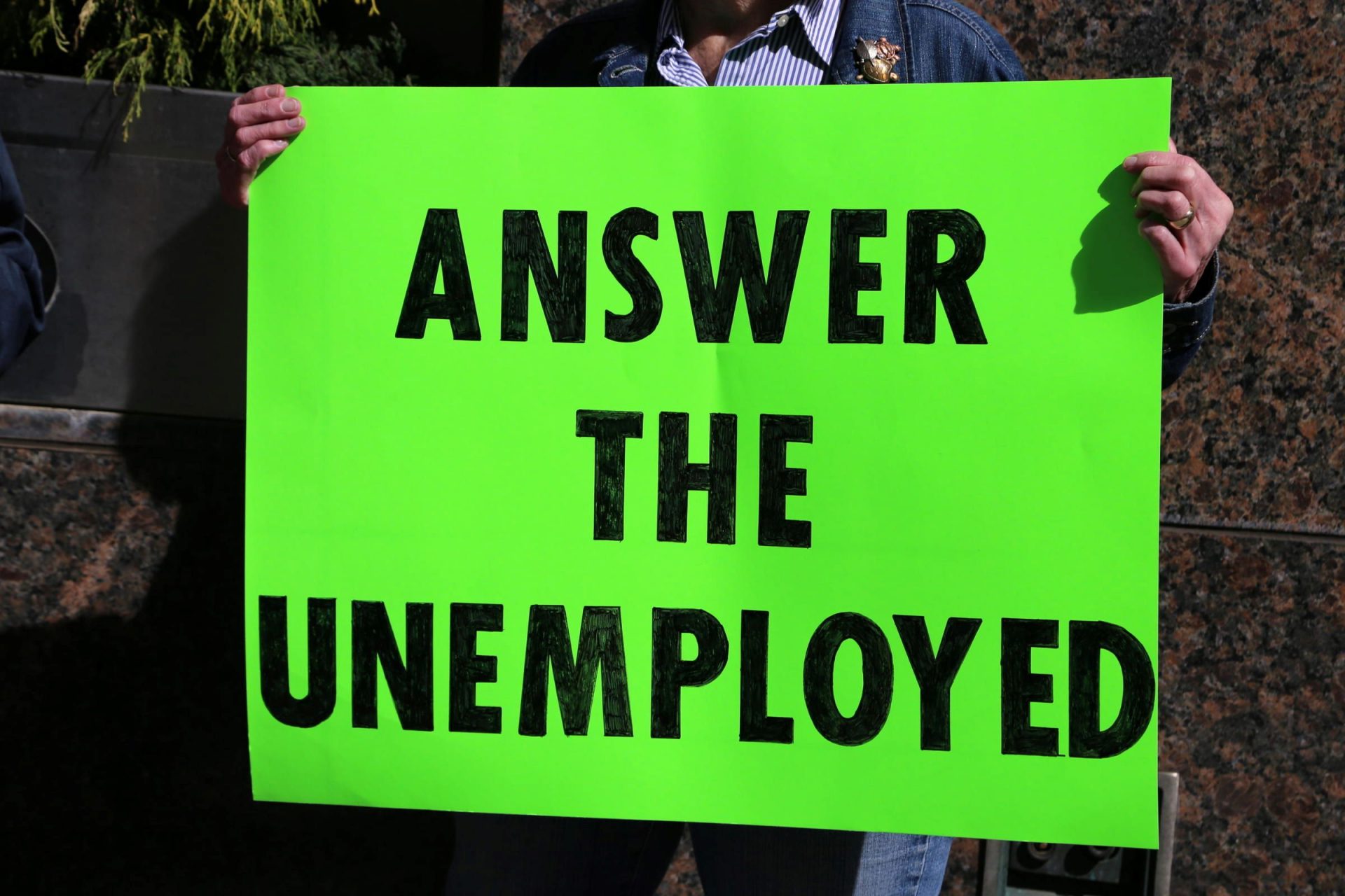 A demonstrator holds a sign about unemployment compensation and the frustrating process many claimants have faced over the past year during a rally downtown on March 10, 2021.