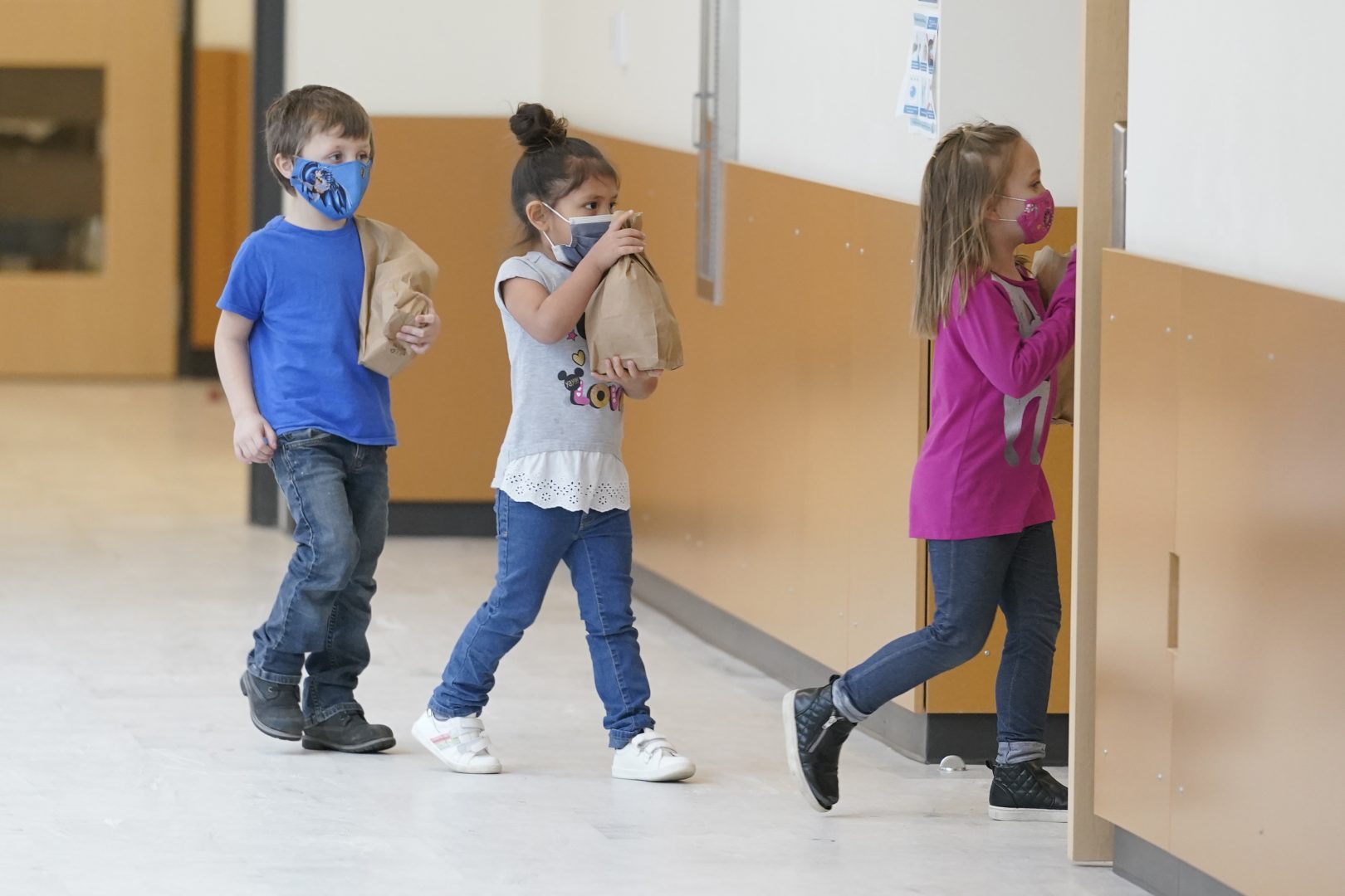Students carry sack lunches as they walk through a hall, Tuesday, Feb. 2, 2021, at Elk Ridge Elementary School in Buckley, Wash.