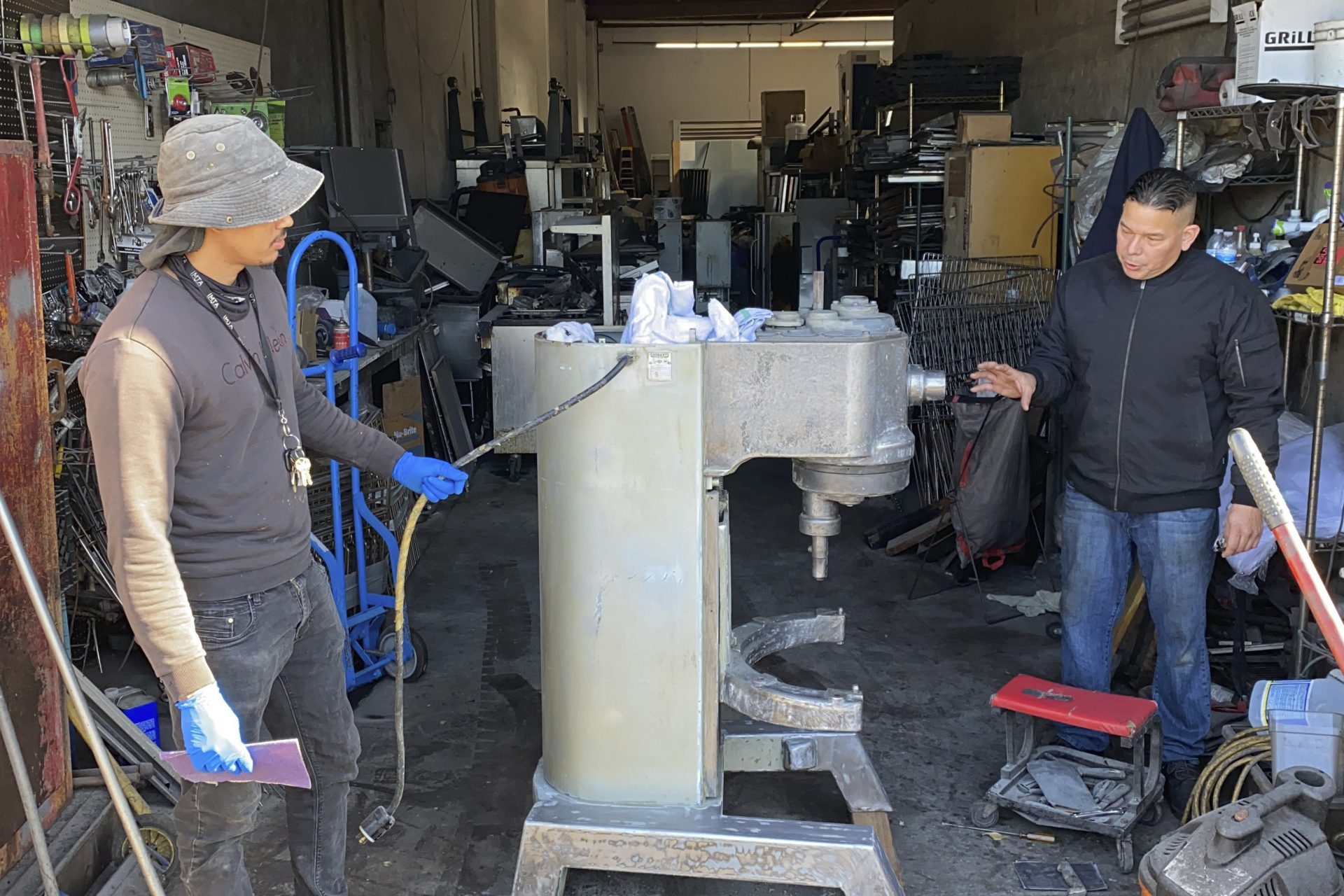 Jose Bonilla Jr., right, talks to an employee about cleaning a used industrial mixer for sale at the warehouse of his family's business, American Restaurant Supply in San Leandro, Calif., on Jan. 14, 2021.