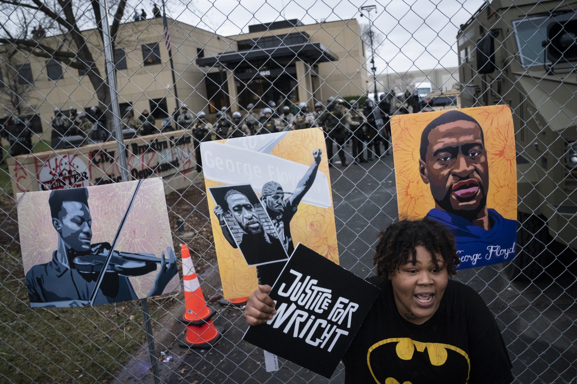 A demonstrator holds a sign along a perimeter fence guarded by law enforcement officers during a protest over Sunday's fatal shooting of Daunte Wright during a traffic stop, outside the Brooklyn Center Police Department, Wednesday, April 14, 2021, in Brooklyn Center, Minn. At right on the fence is an image of George Floyd.