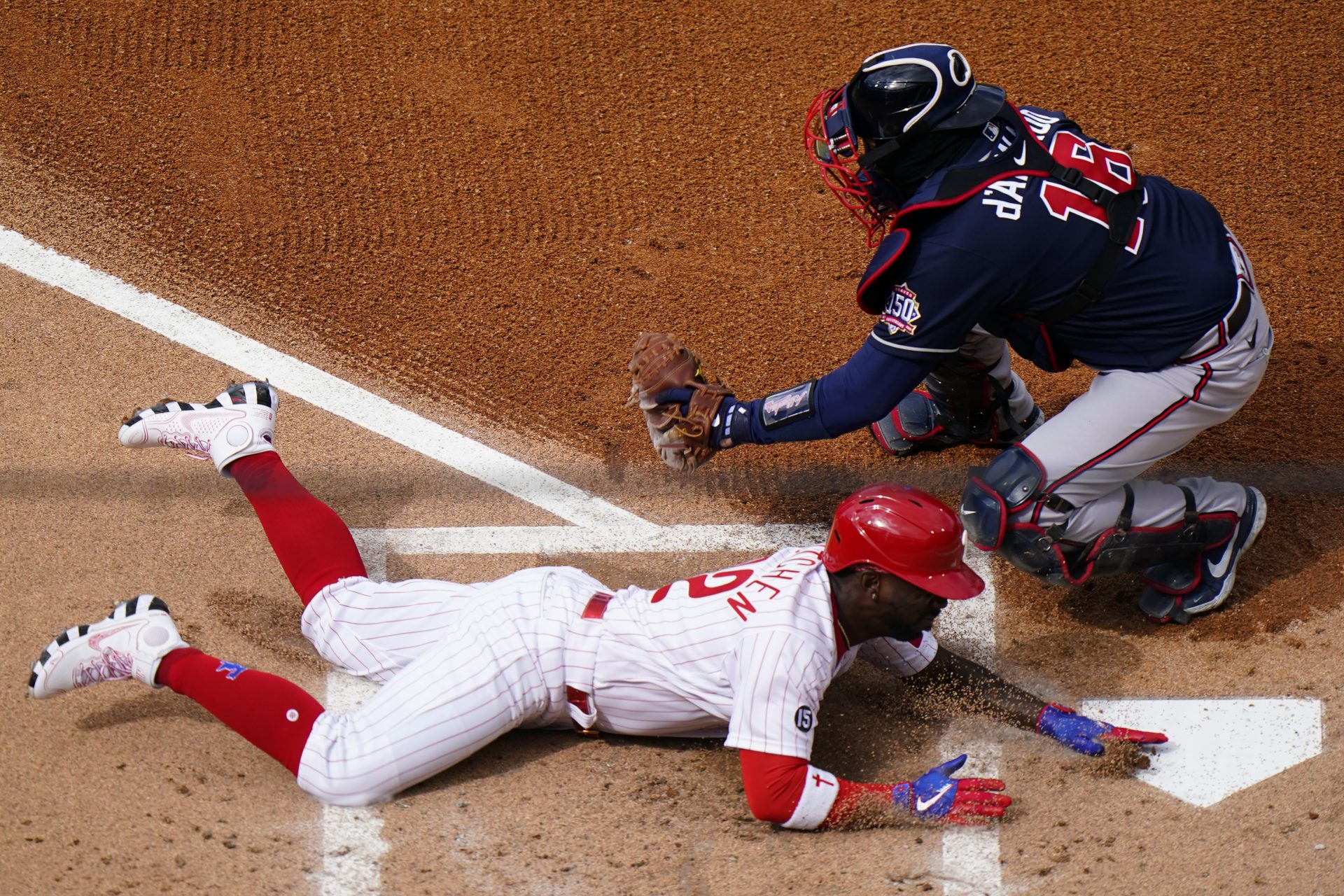 Philadelphia Phillies' Andrew McCutchen, bottom, scores past Atlanta Braves catcher Travis d'Arnaud on an RBI-sacrifice fly by Rhys Hoskins during the first inning of an opening day baseball game, Thursday, April 1, 2021, in Philadelphia.