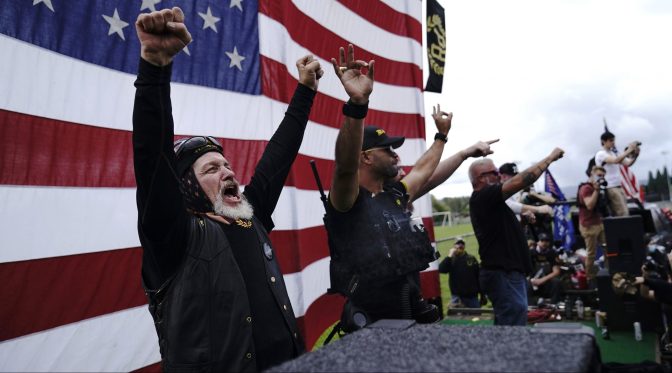 In this Sept. 26, 2020 file photo, members of the Proud Boys, including leader Enrique Tarrio, second from left, gesture and cheer on stage as they and other right-wing demonstrators rally in Portland, Ore.