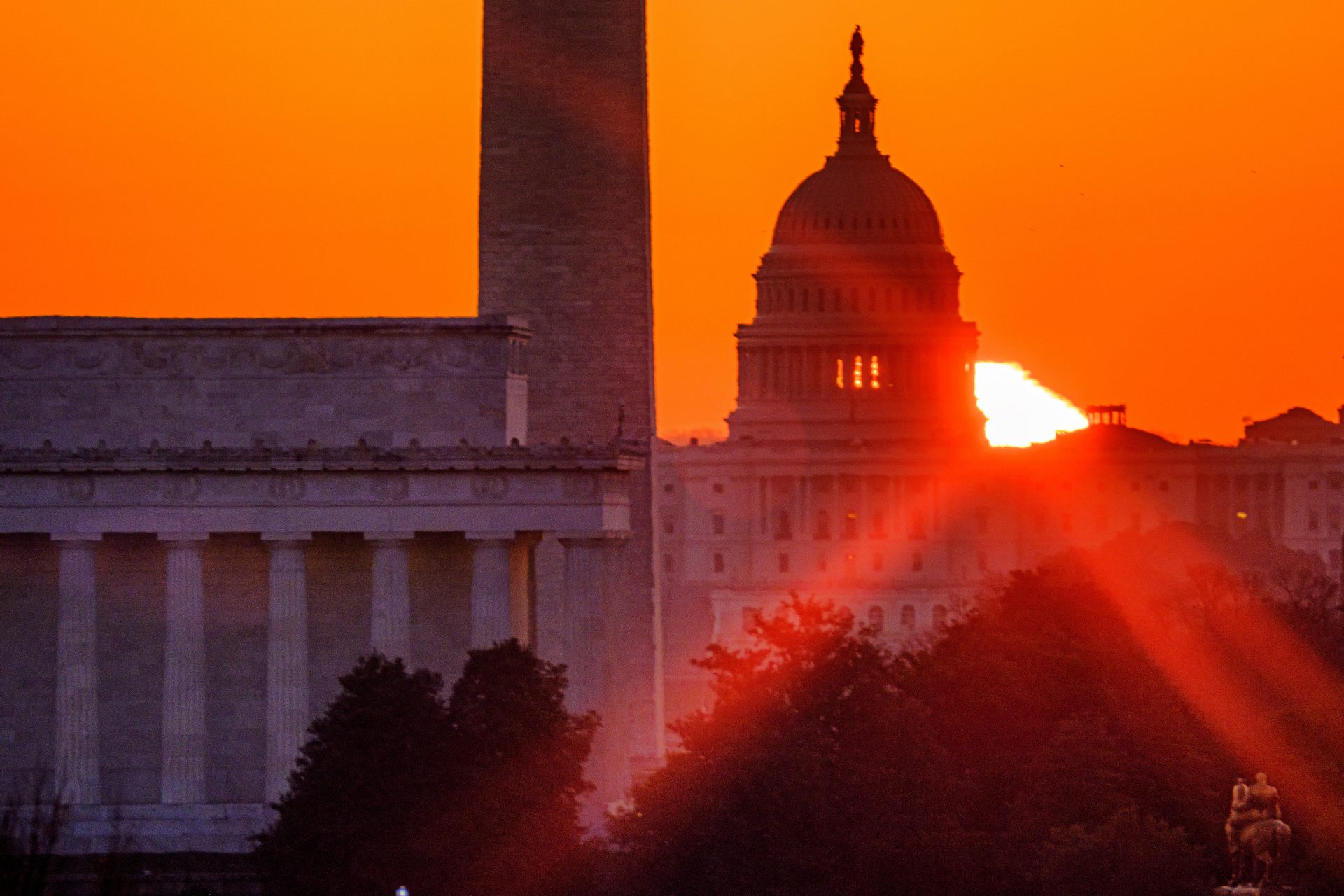 The sun flares through the camera lens as it rises behind the U.S. Capitol building, Washington Monument and the Lincoln Memorial, Monday, March 22, 2021, in Washington.