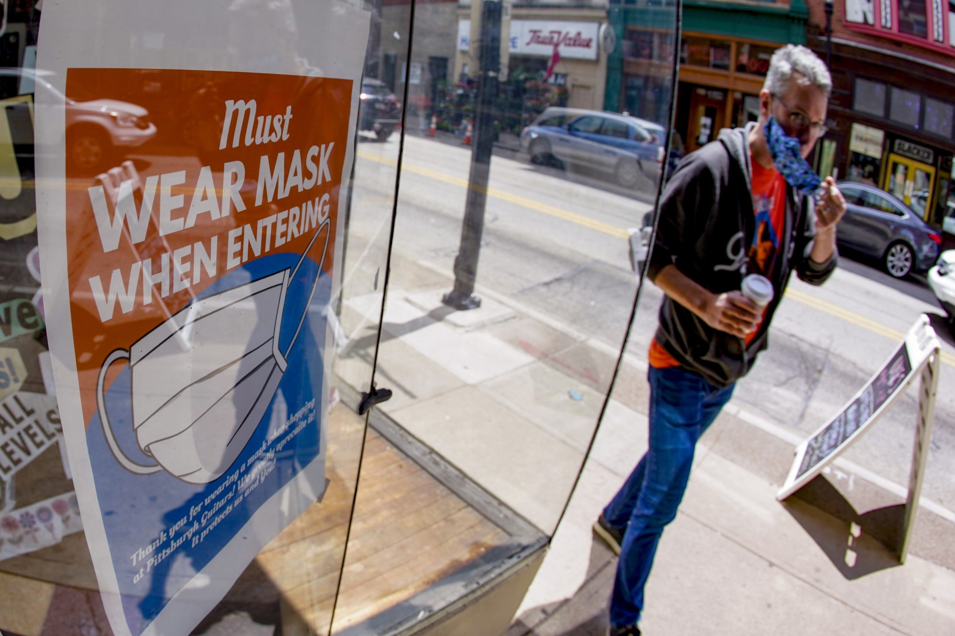 John Bechtold puts his face covering on as he passes his storefront sign that lists COVID-19 protective covering required to enter in his retail shop, Friday, May 14, 2021, in Pittsburgh's South Side neighborhood.