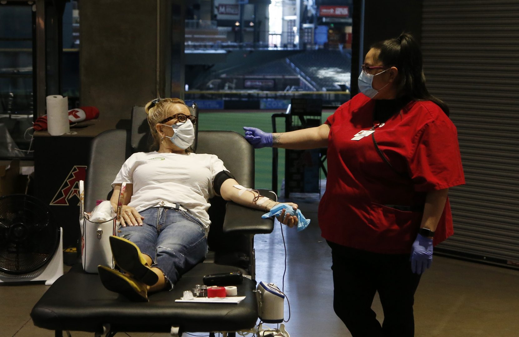 A person donates blood as they talk with an American Red Cross staffer during a Red Cross and Arizona Diamondbacks baseball team blood drive at Chase Field Tuesday, April 28, 2020, in Phoenix. According to the Red Cross, as of April 5, nearly 14,000 Red Cross blood drives have been canceled across the country due to coronavirus concerns, resulting in more than 400,000 fewer blood donations.