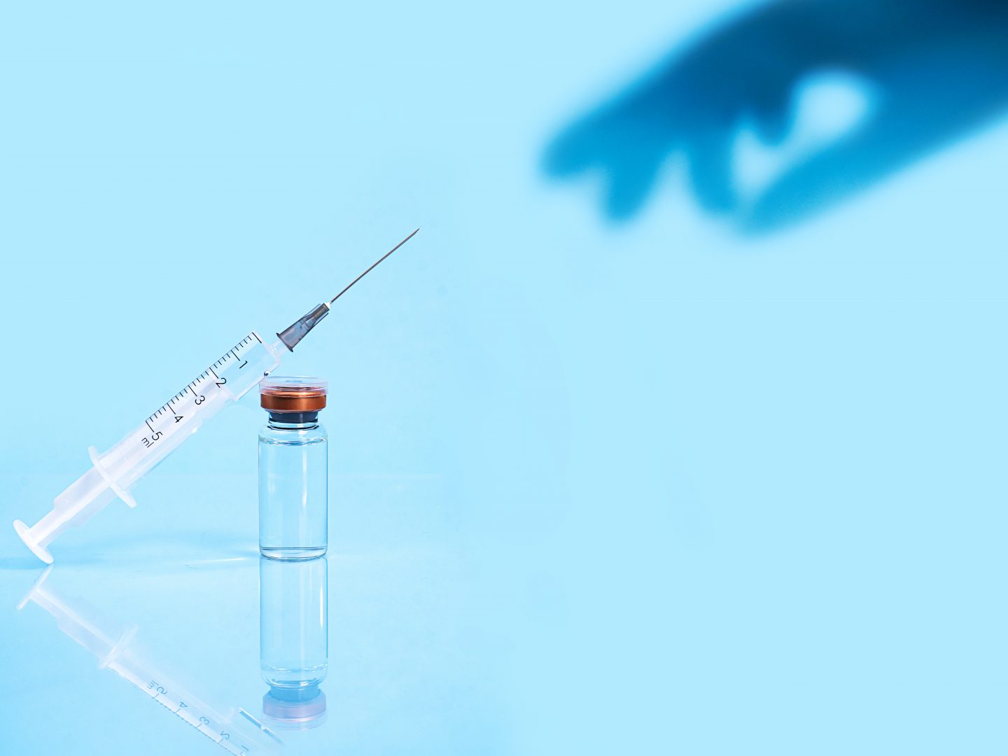 Corona virus medical vaccine. Syringe with needle, vaccine covid-19 liquid and shadow from hand on pastel blue background. Copy space.