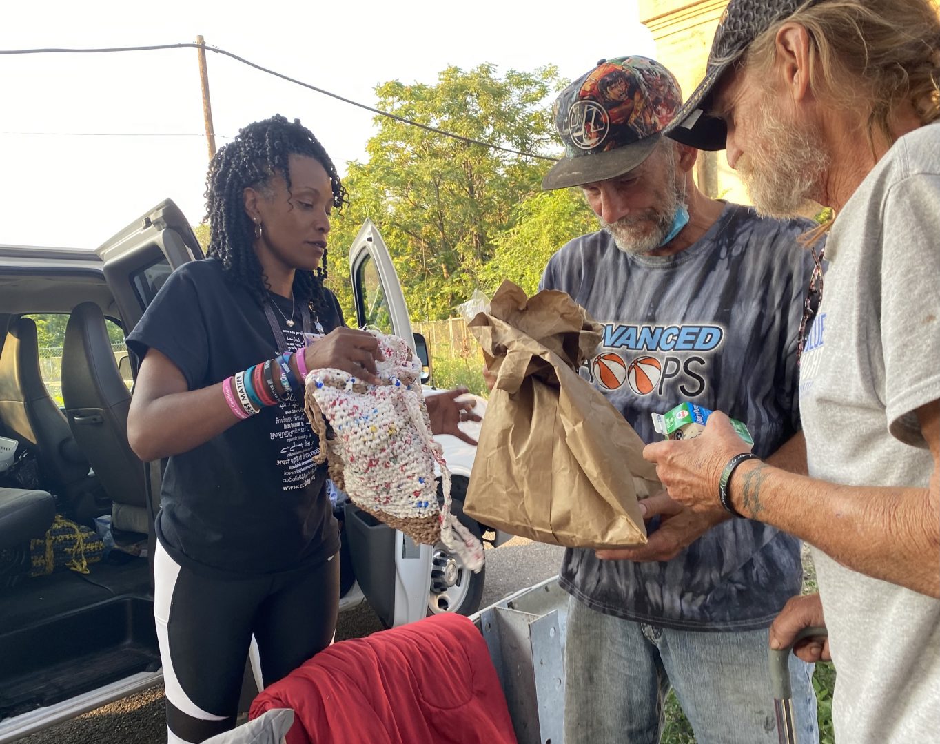 Outreach worker Aisha Mobley, at left, gives food and supplies to men living under a bridge in Harrisburg.