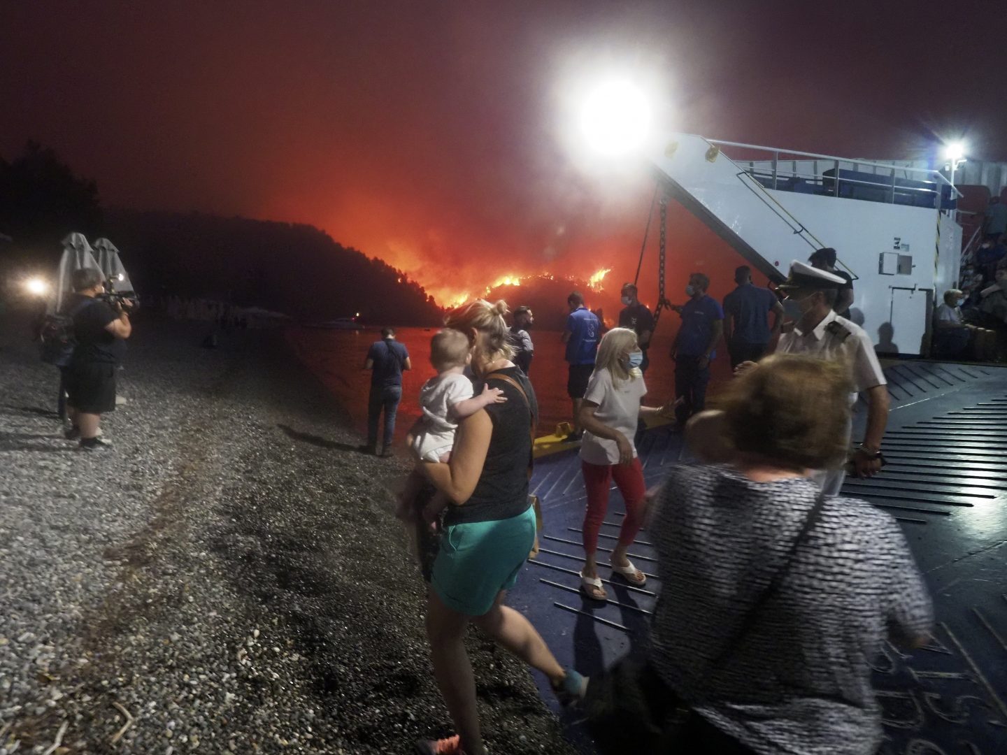 People embark a ferry during an evacuation from Kochyli beach as wildfire approaches near Limni village on the island of Evia, about 160 kilometers (100 miles) north of Athens, Greece, Friday, Aug. 6, 2021. Thousands of people fled wildfires burning out of control in Greece and Turkey on Friday, including a major blaze just north of the Greek capital of Athens that claimed one life, as a protracted heat wave left forests tinder-dry and flames threatened populated areas and electricity installations.