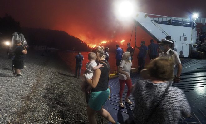 People embark a ferry during an evacuation from Kochyli beach as wildfire approaches near Limni village on the island of Evia, about 160 kilometers (100 miles) north of Athens, Greece, Friday, Aug. 6, 2021. Thousands of people fled wildfires burning out of control in Greece and Turkey on Friday, including a major blaze just north of the Greek capital of Athens that claimed one life, as a protracted heat wave left forests tinder-dry and flames threatened populated areas and electricity installations.