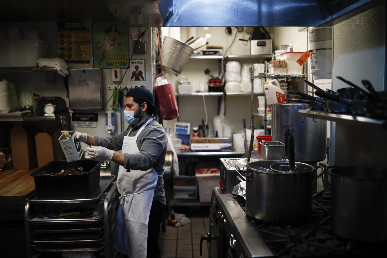 Kitchen worker Misael Cruz, 38, wears a surgical mask and gloves as he prepares food at Little Tong Noodle Shop that is providing meals on a voluntary donation basis for take-out only as authorities restricted gatherings and barred sit-down dining due to coronavirus concerns, Tuesday, March 24, 2020, in New York.