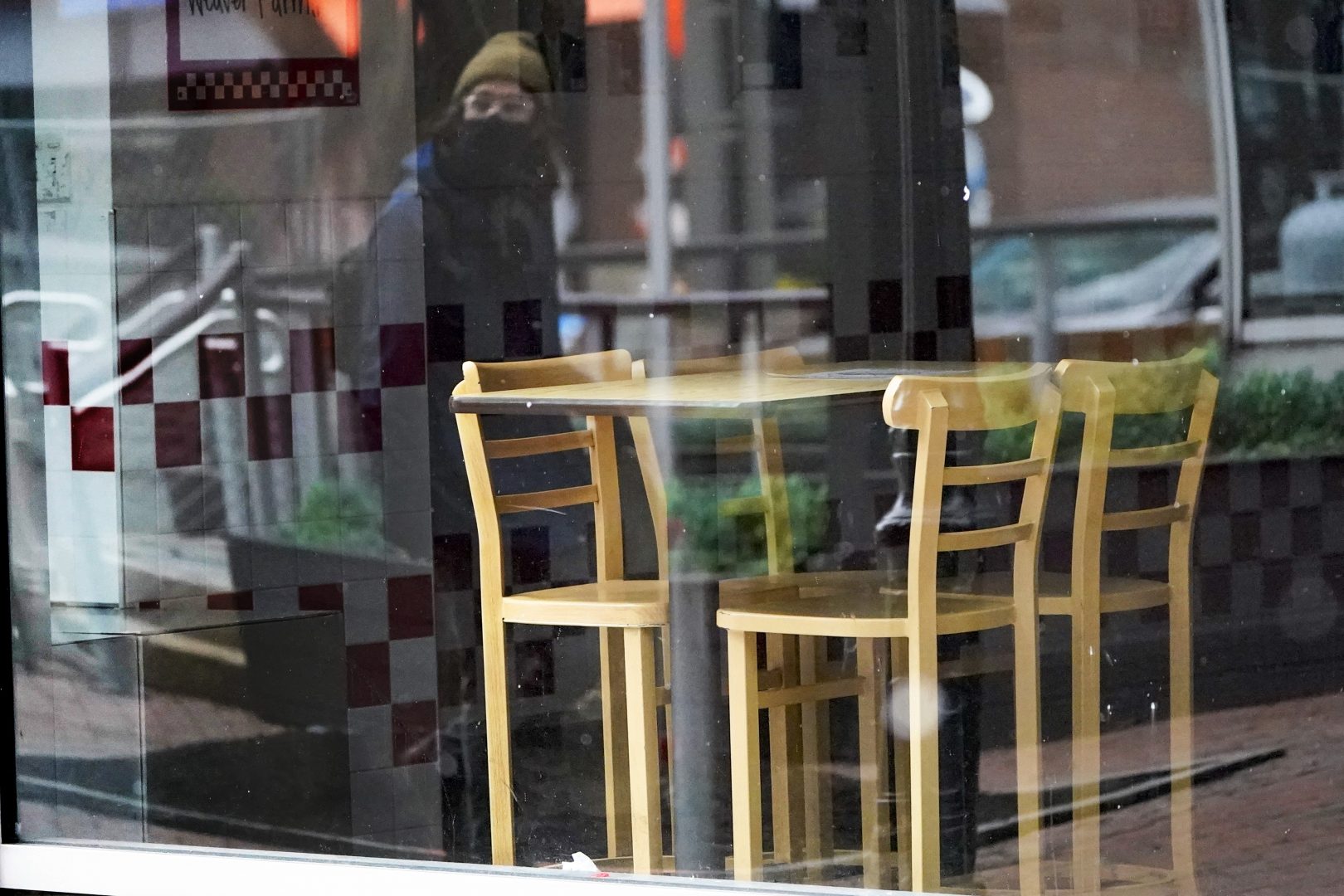 FILE PHOTO: A passer-by wearing a protective mask is reflected in the window of an empty restaurant near Market Square in downtown Pittsburgh, Sunday, Jan. 17, 2021.