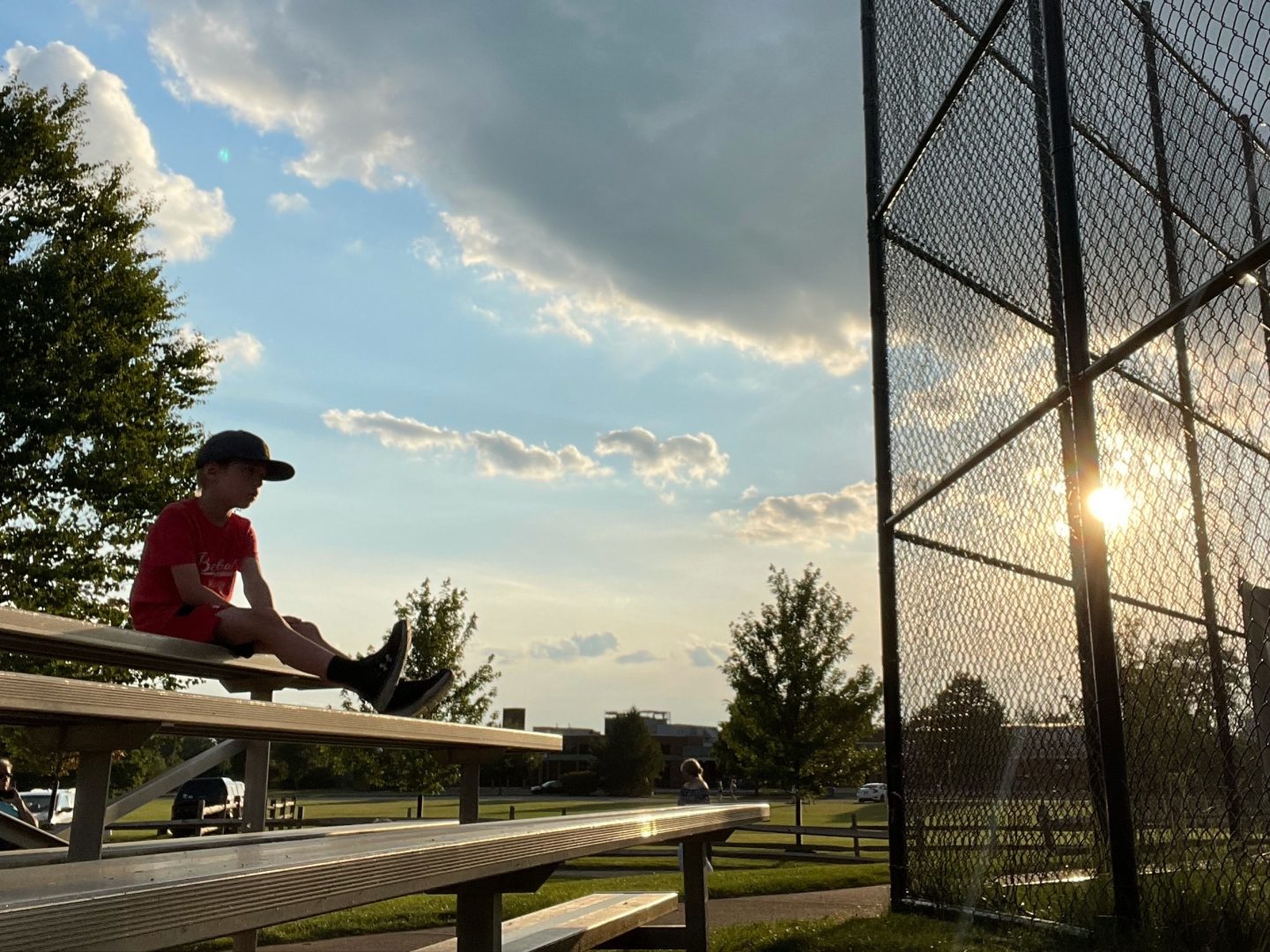 A young boy watches a high-school level municipal league baseball game as the sun sets in Allison Park, Pennsylvania, Thursday, June 24, 2021.