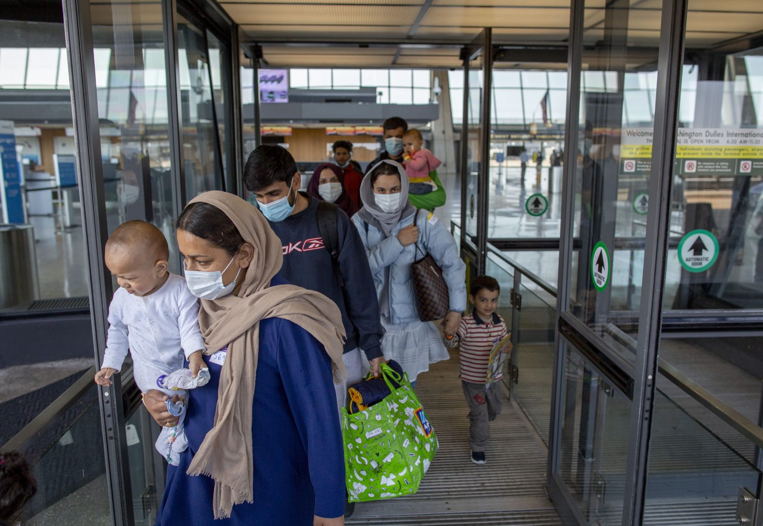 Families evacuated from Kabul, Afghanistan, walk through the terminal to board a bus after they arrived at Washington Dulles International Airport, in Chantilly, Va., on Saturday, Aug. 28, 2021.