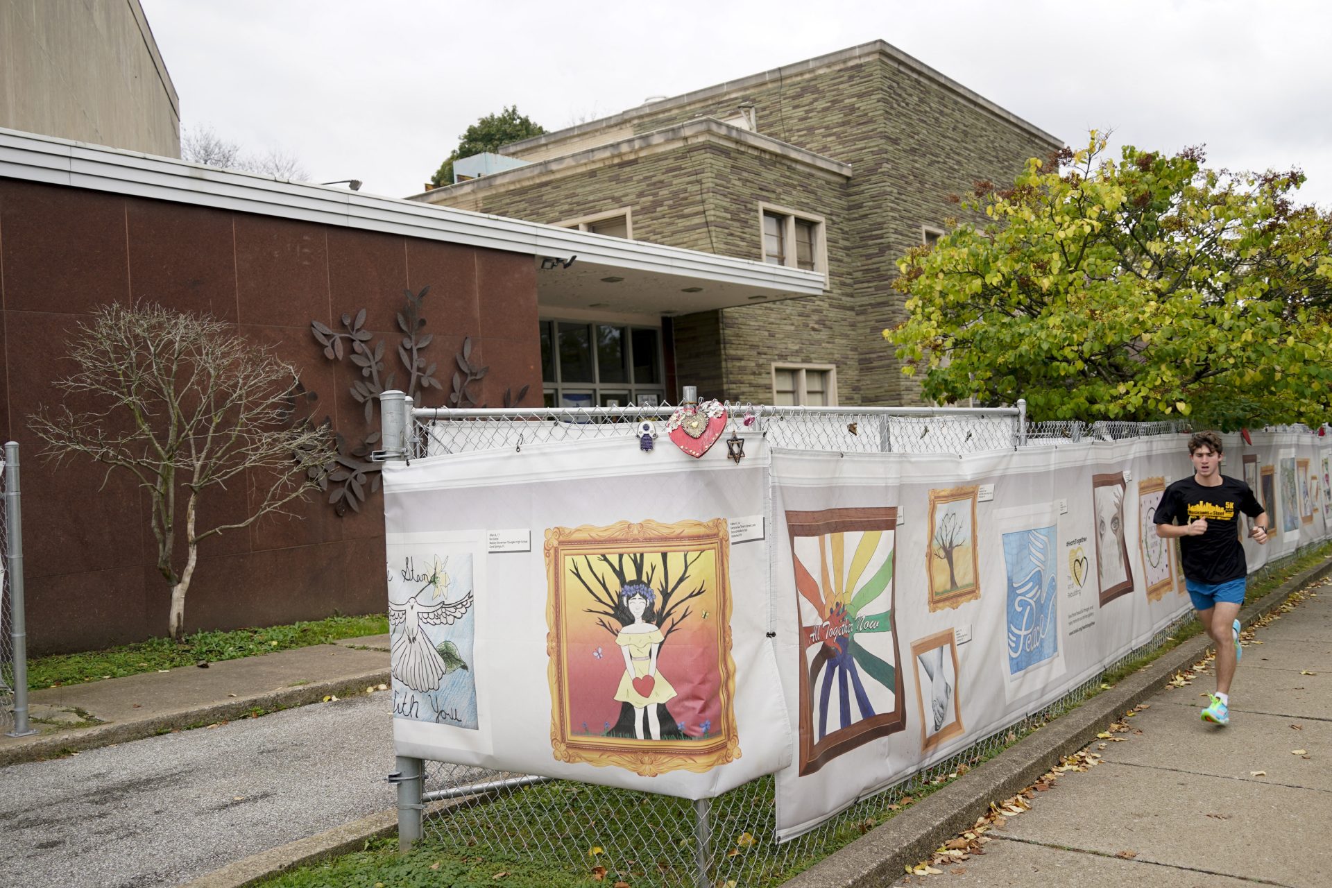 This photo from Oct. 16, 2021, shows the dormant landmark Tree of Life synagogue as a man jogs past the fencing with artwork submitted by Pittsburgh area school students in Pittsburgh's Squirrel Hill neighborhood.