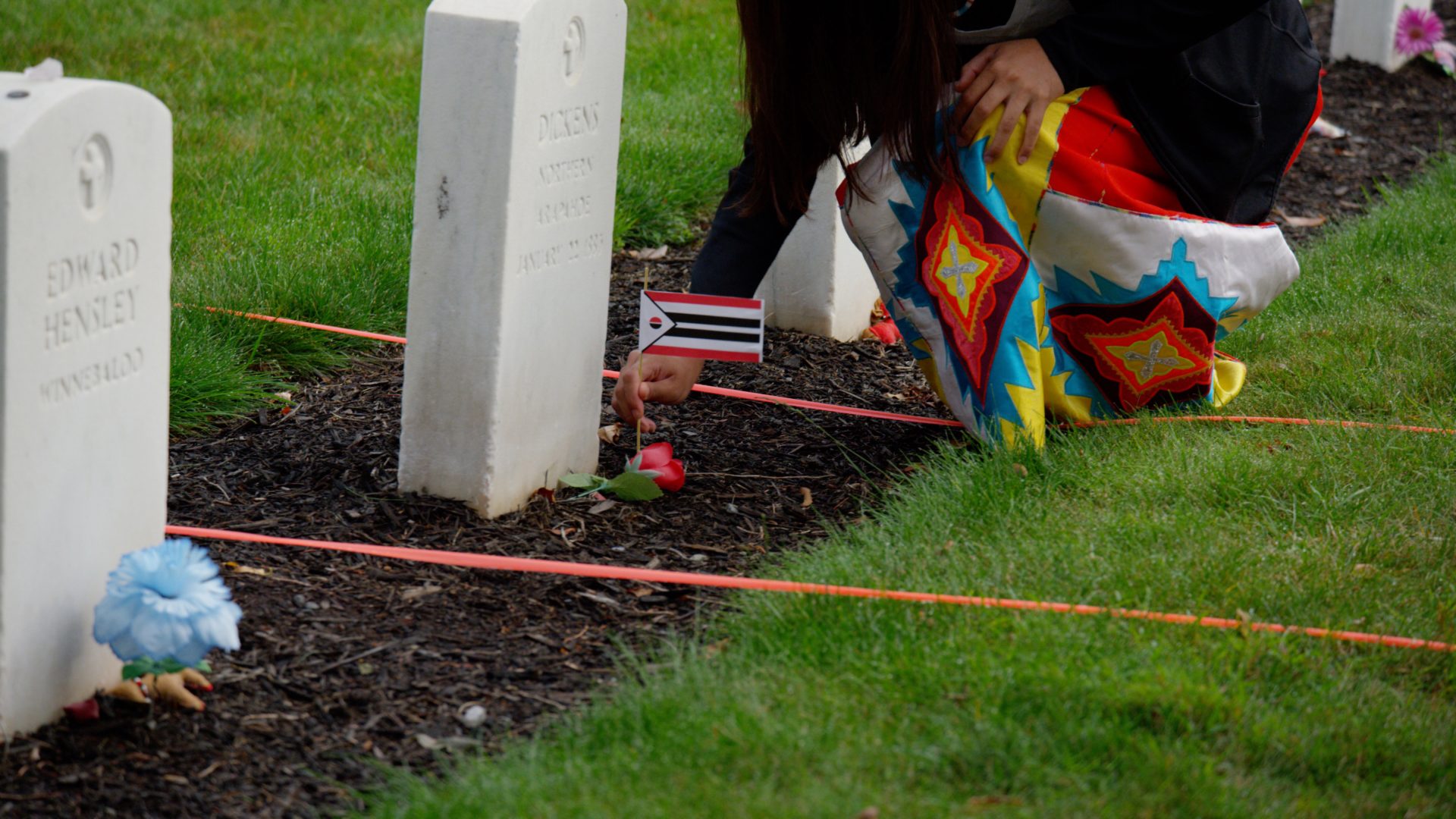 Loveeda White places an Arapaho flag at the base of Little Chief/Dickens Nor's headstone in the Carlisle Indian Cemetery, Carlisle PA, 2017