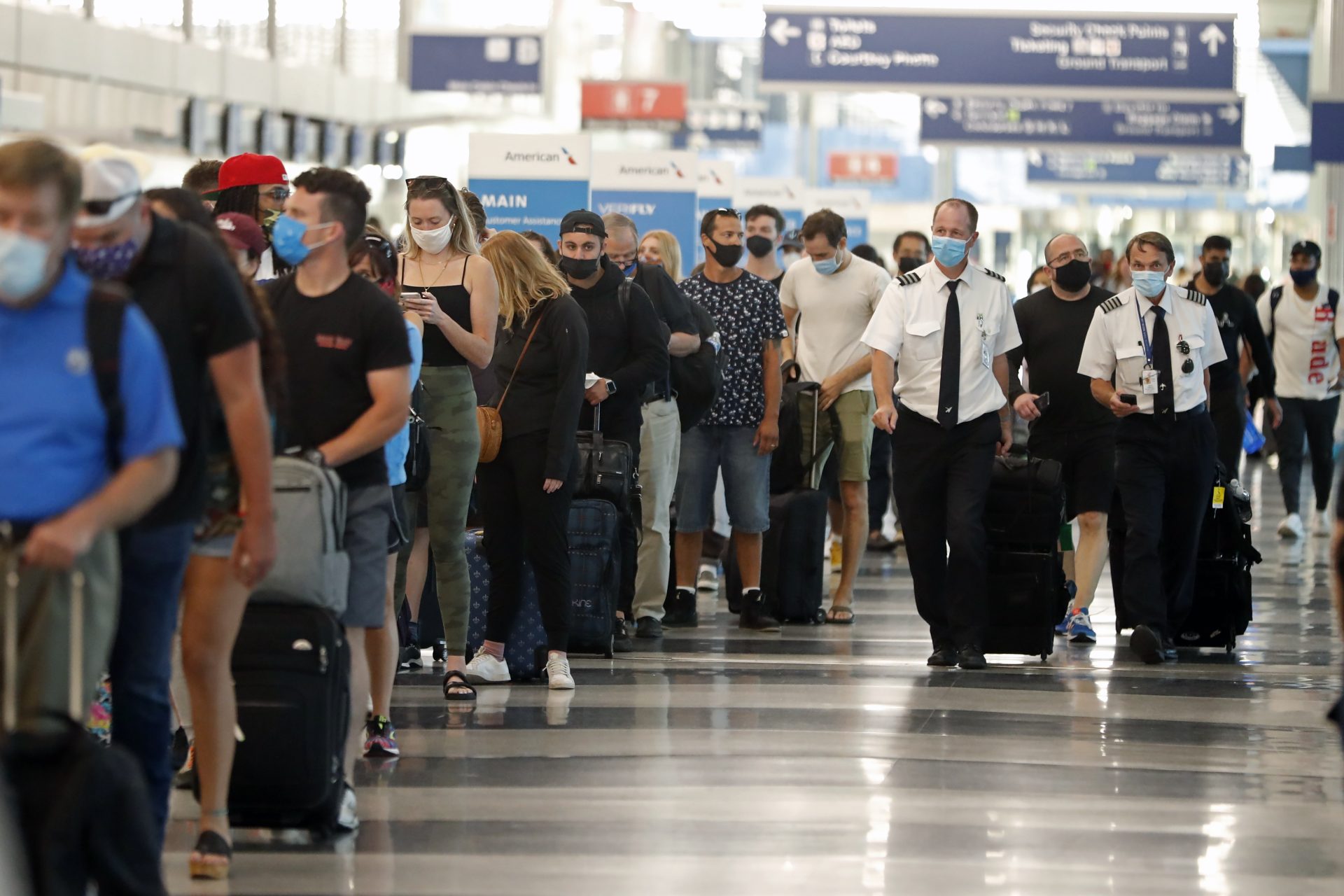 Two airplane pilots pass by a line of passengers while waiting at a security check-in line at O'Hare International Airport in Chicago, ahead of Fourth of July weekend, July 1, 2021.