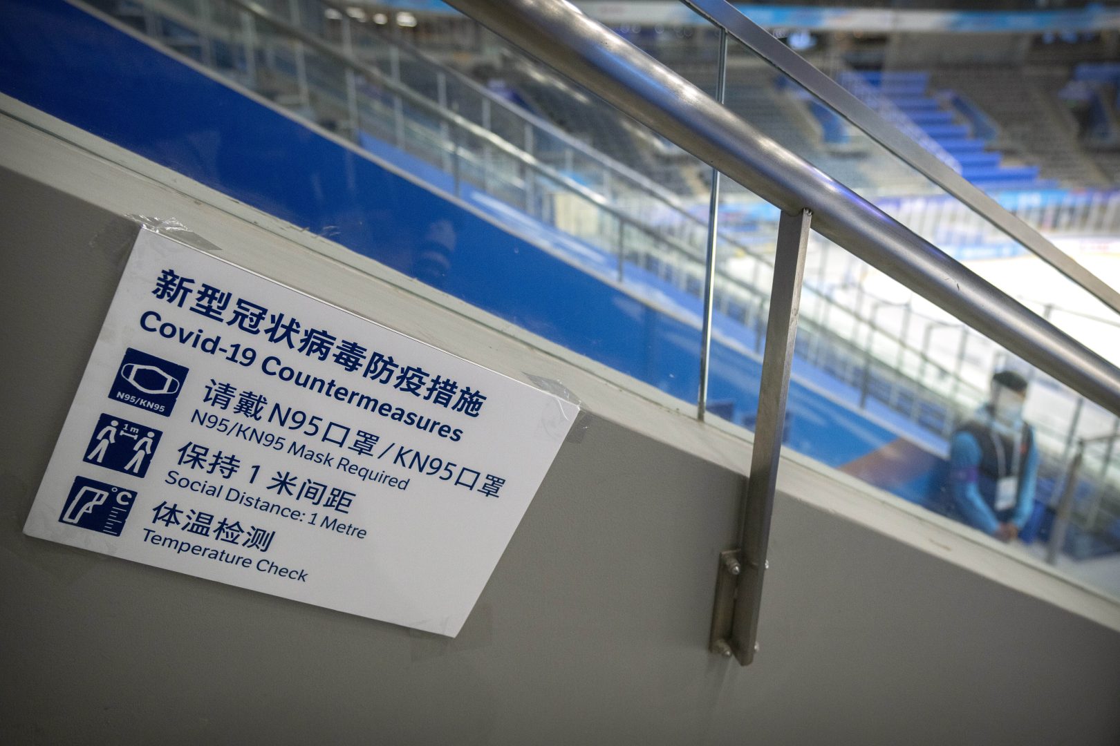 FILE - A staff member stands near a sign outlining COVID-19 protection measures during the Experience Beijing Ice Hockey Domestic Test Activity, a test event for the 2022 Beijing Winter Olympics, at the National Indoor Stadium in Beijing, on Nov. 10, 2021.  The prevention protocols will be similar to those at the Tokyo Games this summer, but tighter. It won't be a stretch for Beijing organizers, with China having maintained its zero-tolerance policy to the virus nationally since early in the pandemic. (AP Photo/Mark Schiefelbein, File)