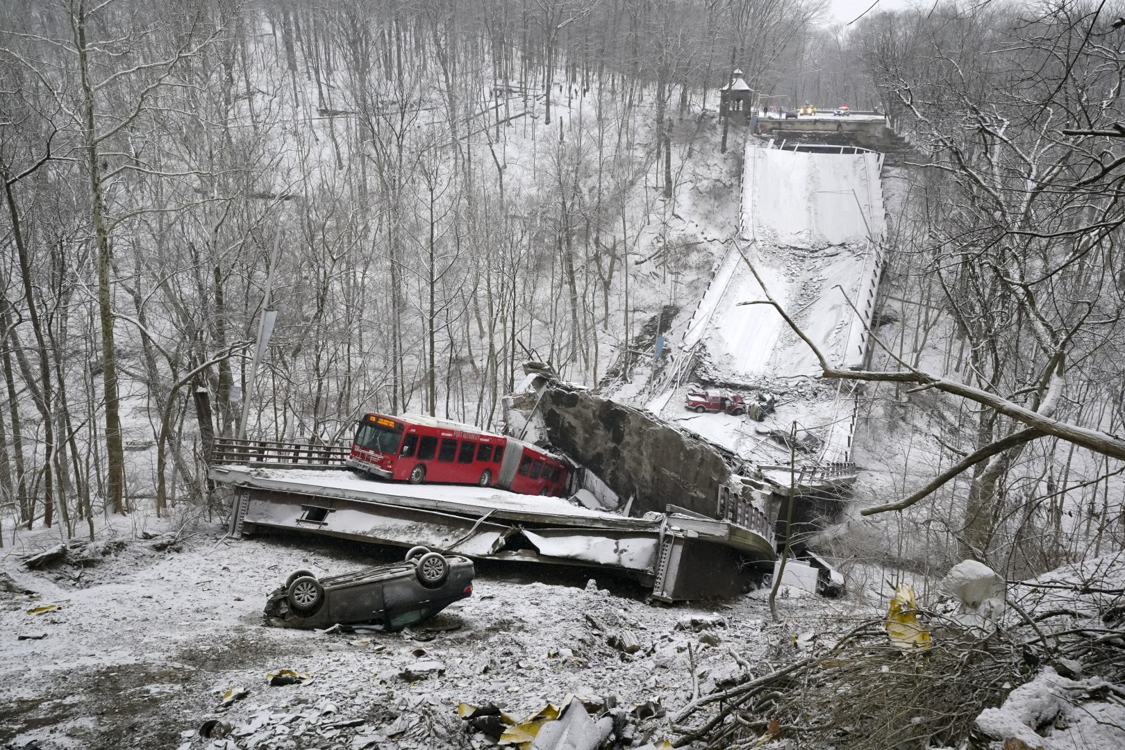 A Port Authority bus that was on a bridge when it collapsed Friday Jan. 28, 2022, is visible in Pittsburgh's East End.  A two-lane bridge collapsed in Pittsburgh early Friday, prompting rescuers to rappel nearly 150 feet (46 meters) while others formed a human chain to help rescue multiple people from a dangling bus.(AP Photo/Gene J. Puskar)