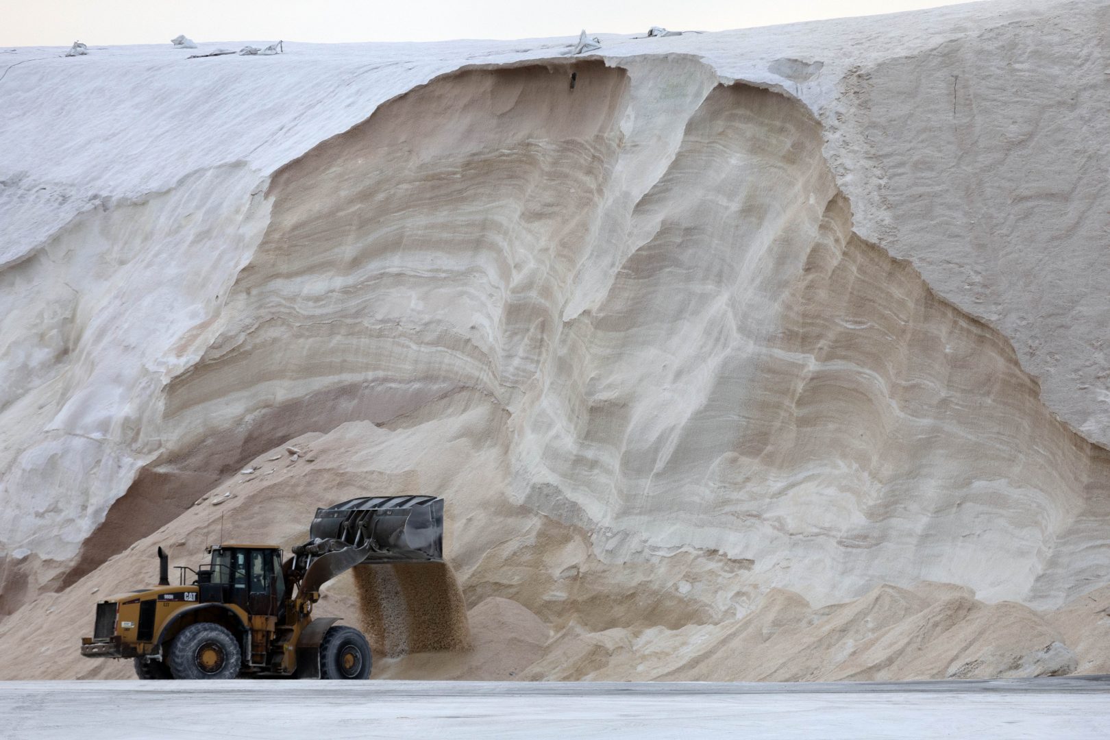 A front-end loader works in front of a pile of road salt, Friday, Jan. 28, 2022, in Chelsea, Mass. Residents and officials in the Northeast and mid-Atlantic regions of the U.S. are bracing for a powerful winter storm expected to produce blizzard conditions Friday and Saturday. (AP Photo/Michael Dwyer)