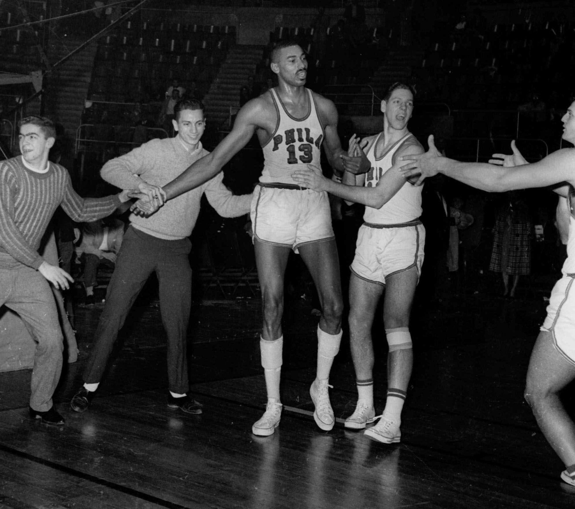 Unidentified fans and teammates rush onto court to congratulate Philadelphia Warriors Wilt Chamberlain (13) at Hershey, Pa., March 2, 1962, after he scored his 100th point for an NBA record.