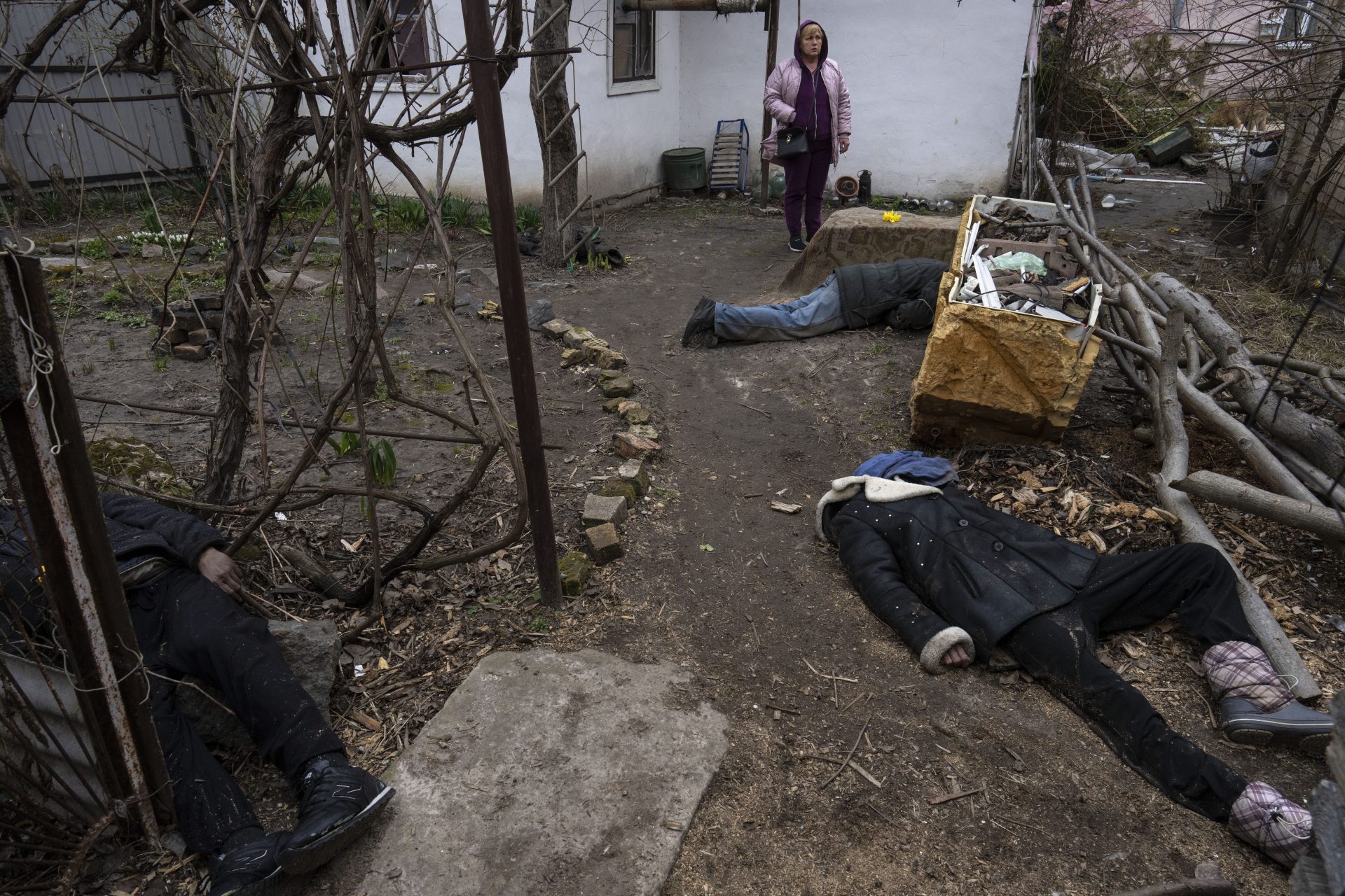 A woman stands next to three people killed in the courtyard of a house in Bucha, on the outskirts of Kyiv, Ukraine, Tuesday, April 5, 2022.