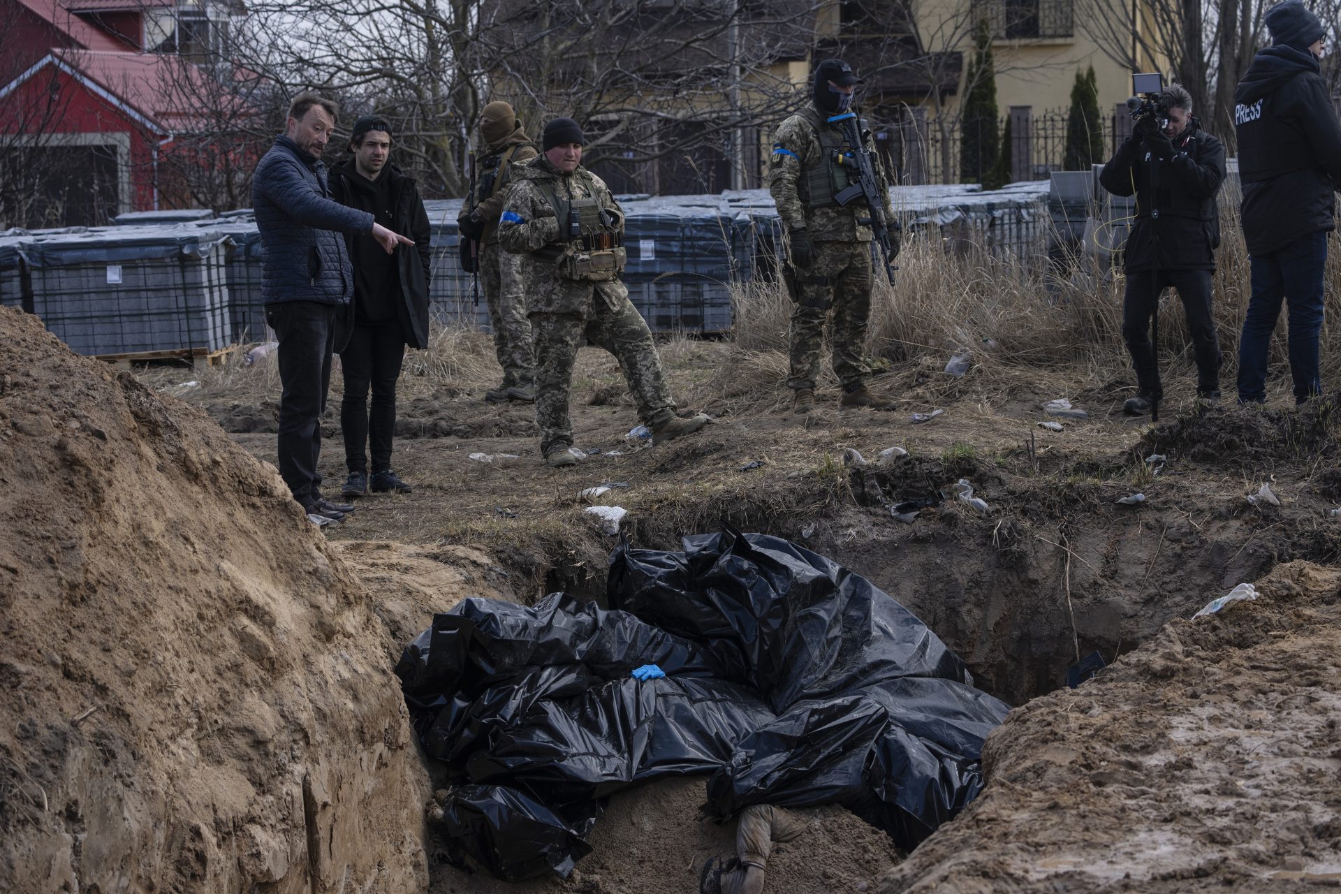 People stand next to a mass grave in Bucha, on the outskirts of Kyiv, Ukraine, April 4, 2022. AP journalists saw dozens of bodies in Bucha, many of them shot at close range, and some with their hands tied behind them