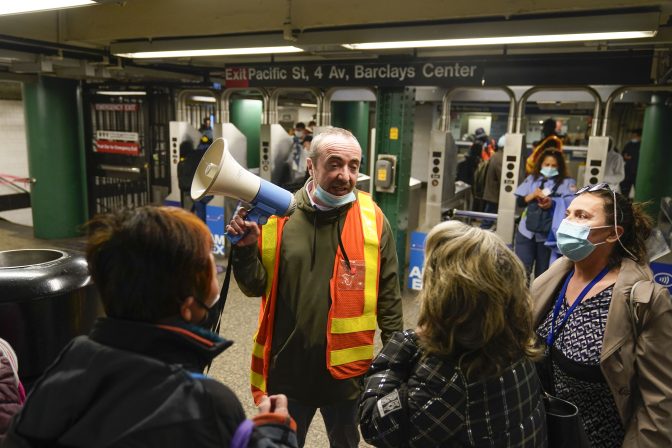 An MTA official helps to direct commuters at a subway station in New York, Tuesday, April 12, 2022. Multiple people were shot and injured Tuesday at a subway station in New York City during a morning rush hour attack that left wounded commuters bleeding on a train platform.