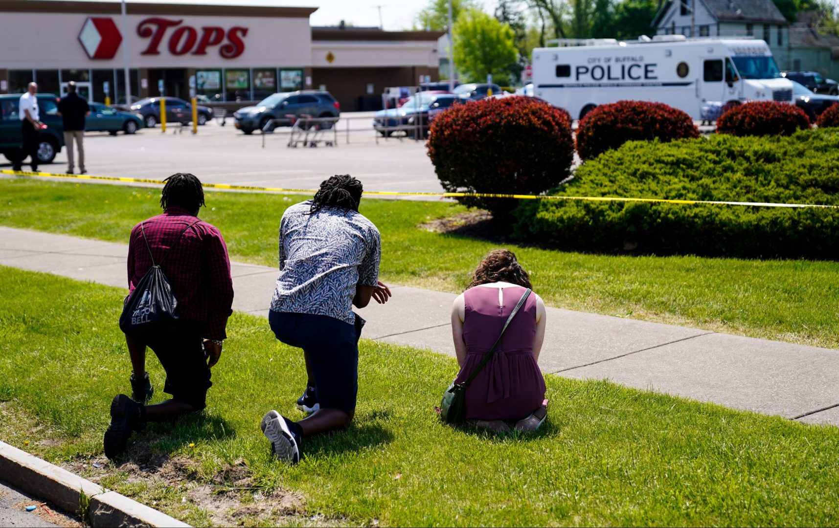 People pray outside the scene of Saturday's shooting at a supermarket, in Buffalo, N.Y., Sunday, May 15, 2022. The shooting is the latest example of something that's been part of U.S. history since the beginning: targeted racial violence.