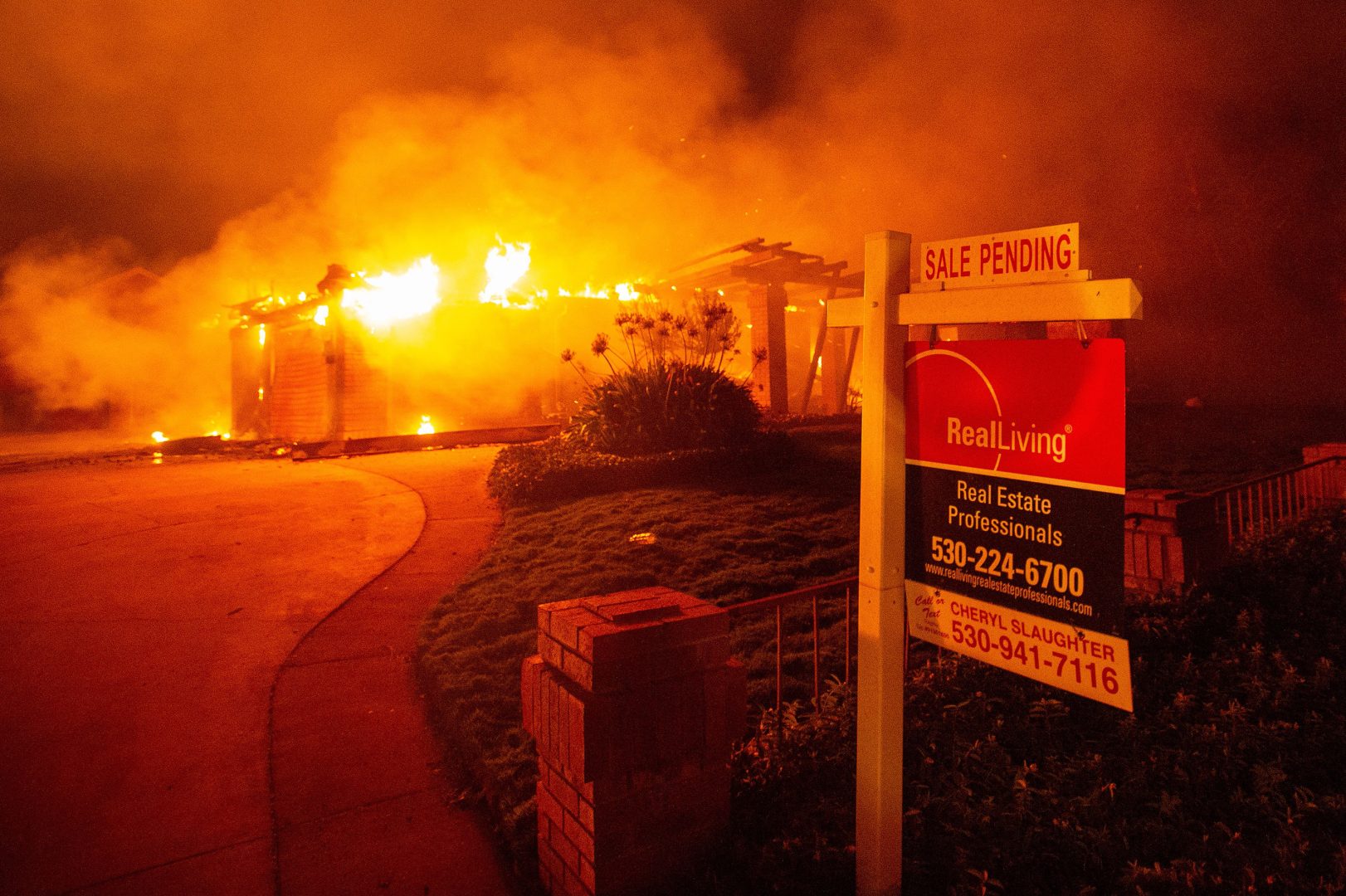 A real estate sign is seen in front of a burning home during the Carr fire in Redding, California on July 27, 2018. - One firefighter has died and at least two others have been injured as wind-whipped flames tore through the region. 
