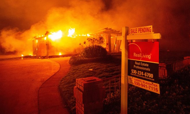 A real estate sign is seen in front of a burning home during the Carr fire in Redding, California on July 27, 2018. - One firefighter has died and at least two others have been injured as wind-whipped flames tore through the region. 