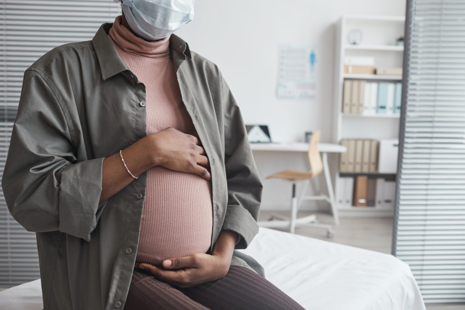 Close-up of pregnant woman in mask sitting at doctor's office during her visit