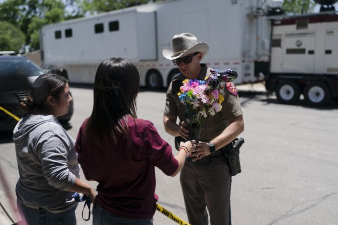 A state trooper takes flowers from two people from the neighborhood to place them at a makeshift memorial honoring the victims killed in Tuesday's shooting at Robb Elementary School in Uvalde, Texas, Wednesday, May 25, 2022.