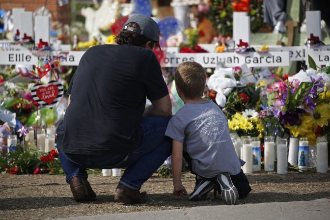 A man and a child pay their respects at a memorial outside Robb Elementary School to honor the victims killed in a school shooting in Uvalde, Texas Sunday, May 29, 2022.