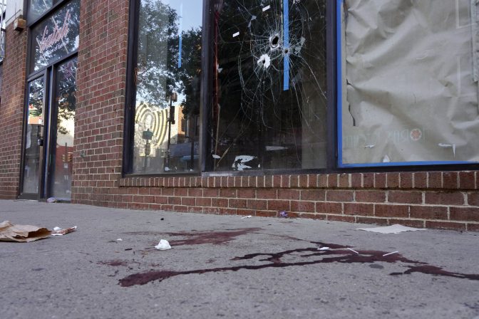 Blood is seen at the scene of a fatal overnight shooting on South Street in Philadelphia, Sunday, June 5, 2022, where bullet holes on a storefront window from a prior shooting can also be seen.