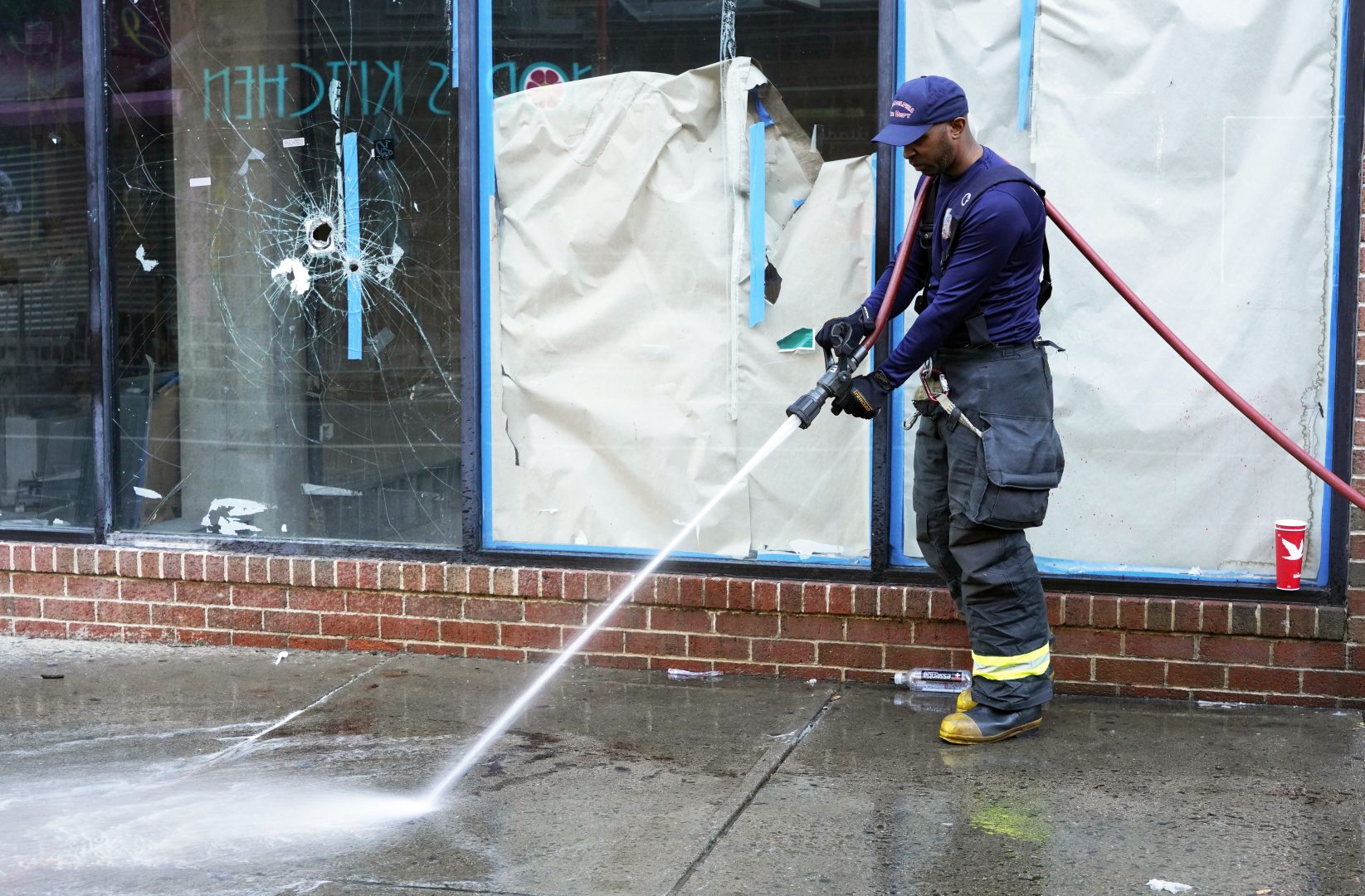  A Philadelphia fireman washes blood off the sidewalk at the scene of a fatal overnight shooting on South Street in Philadelphia, Sunday, June 5, 2022, where bullet holes on a storefront window from a prior shooting can also be seen. 