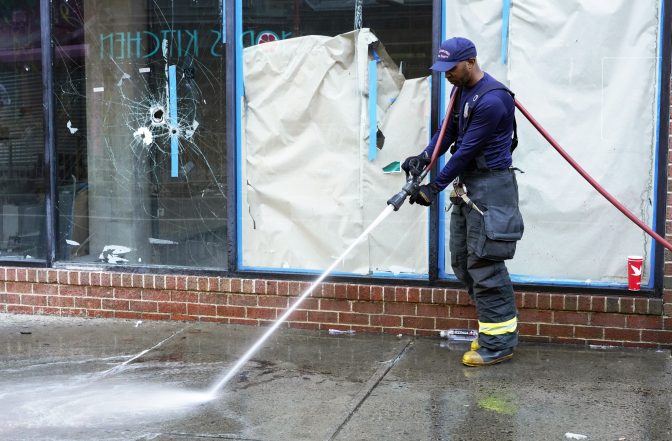 A Philadelphia fireman washes blood off the sidewalk at the scene of a fatal overnight shooting on South Street in Philadelphia, Sunday, June 5, 2022, where bullet holes on a storefront window from a prior shooting can also be seen.