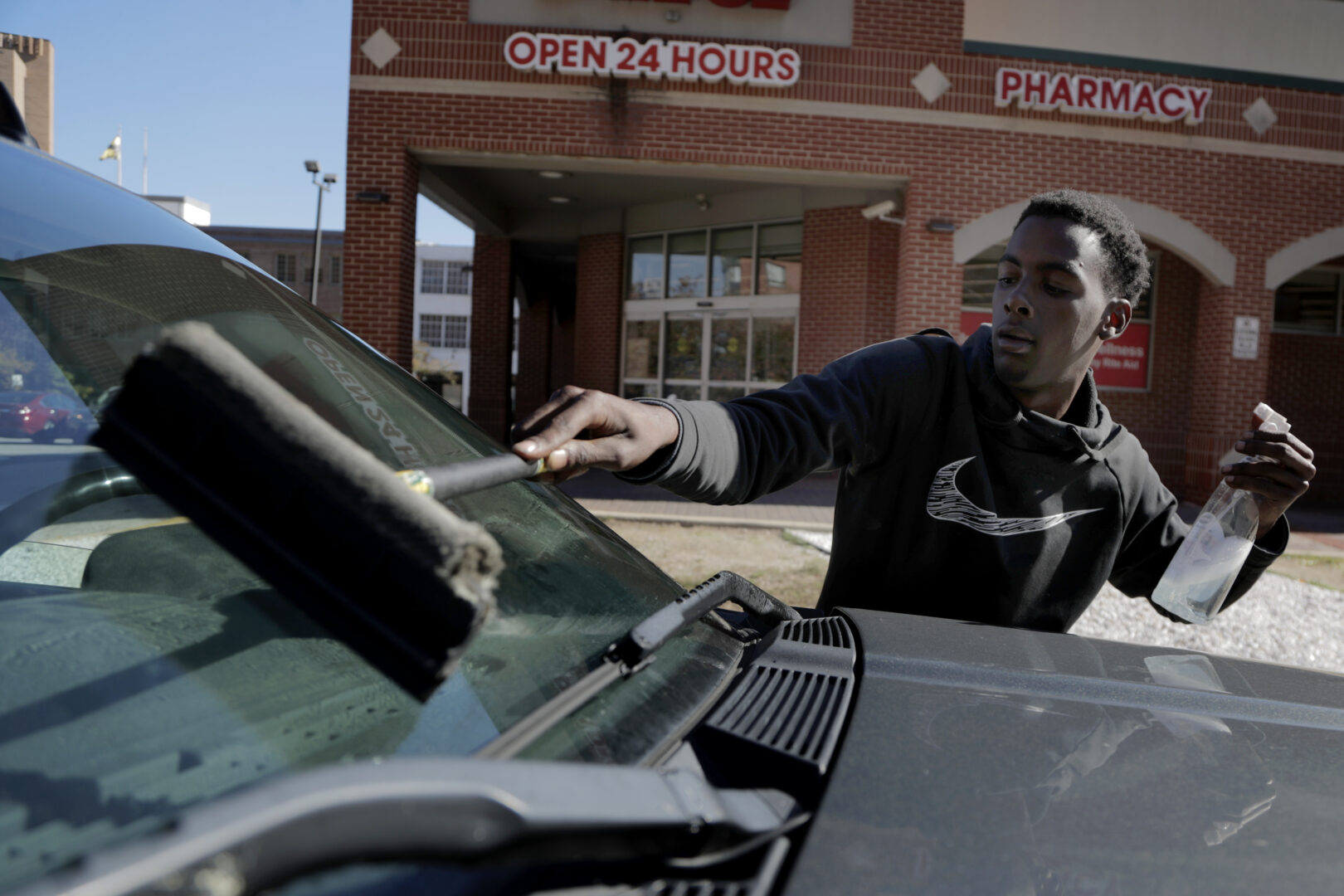 In this Thursday, Oct. 24, 2019 photo, Nathaniel Silas squeegees a windshield of a truck stopped at a red light in Baltimore. A debate over Baltimore's so-called squeegee kids is reaching a crescendo as the city grapples with issues of crime and poverty and a complicated history with race relations. Officials estimate 100 squeegee kids regularly work at intersections citywide, dashing into the street as red lights hit to clean windshields in exchange for cash from drivers. (AP Photo/Julio Cortez)