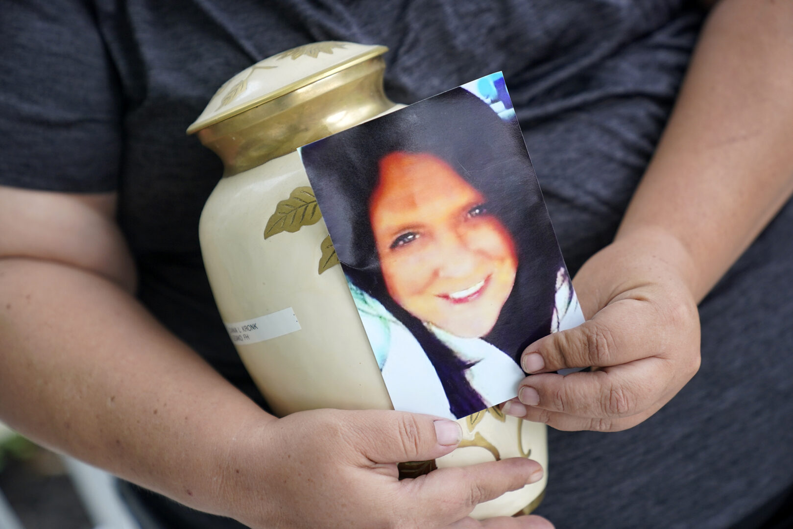 Kelly Titchenell sits on her porch in Mather, Pa., holding a photo of her mother Diania Kronk, and an urn containing her mother's ashes, Thursday, July 7, 2022. A Greene County, Pa., detective last week filed charges against 911 operator Leon “Lee” Price, 50, of Waynesburg, in the July 2020 death of Diania Kronk, 54, based on Price's reluctance to dispatch help without getting more assurance that Kronk would actually go to the hospital. (AP Photo/Gene J. Puskar)