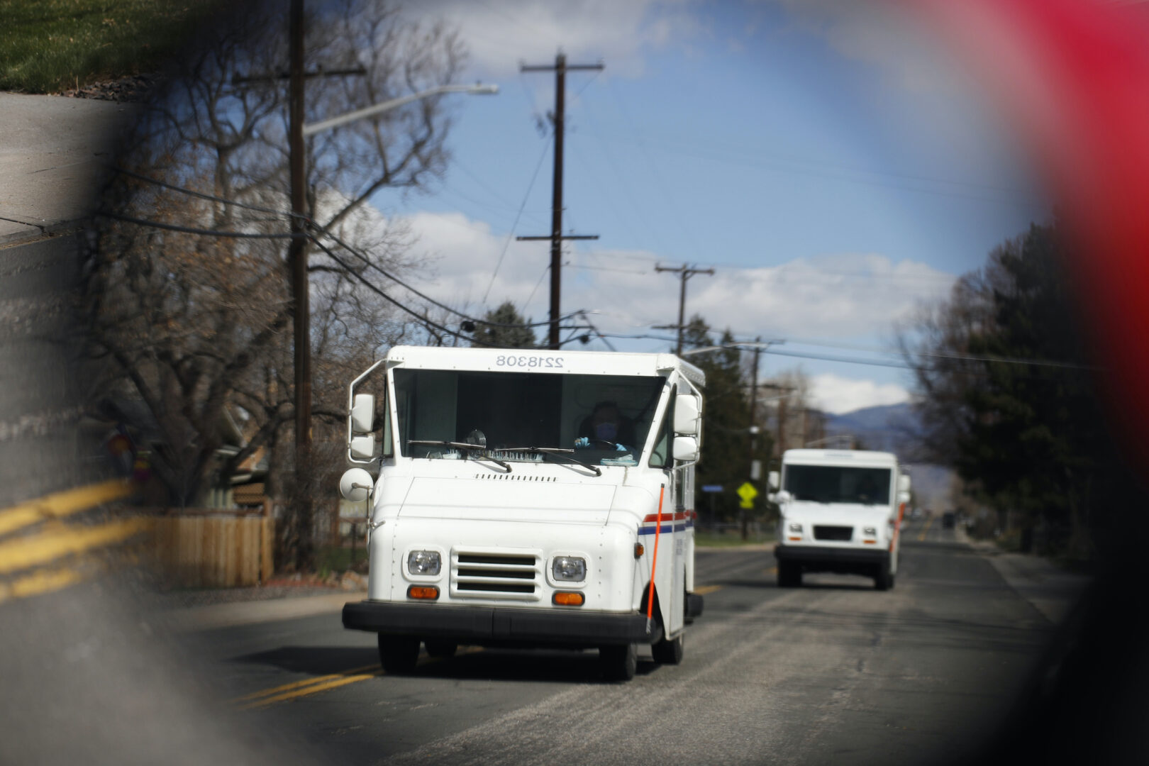 United States Post Office delivery trucks are reflected in the side mirror of a vehicle as postal delivers set off on their daily rounds  as a statewide stay-at-home order remains in effect in an effort to reduce the spread of the new coronavirus Tuesday, March 31, 2020, in  Arvada, Colo. The new coronavirus causes mild or moderate symptoms for most people, but for some, especially older adults and people with existing health problems, it can cause more severe illness or death. (AP Photo/David Zalubowski)