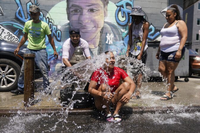 Jennifer Pagan, center, reacts as she sits in front of an open fire hydrant in The Bronx section of New York, Friday, July 22, 2022.