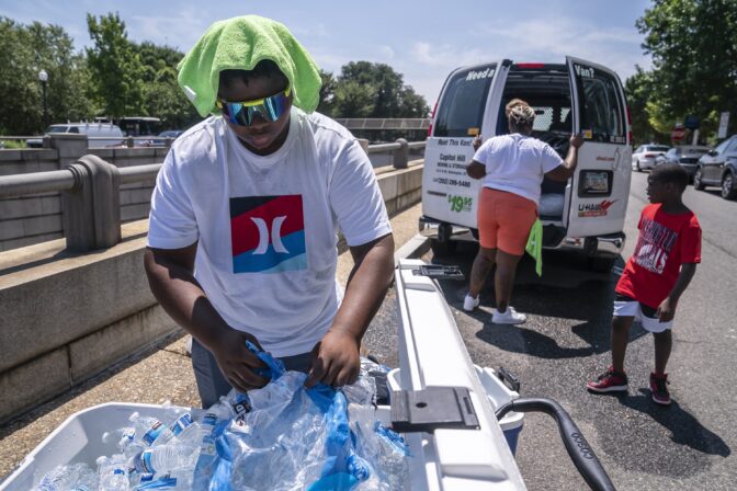 Amir Brown, 15, left, loads a cooler with ice and water while his mother Nicole Brown, center, sets up her beverage stand near the National Mall on Friday, July 22, 2022, in Washington.
