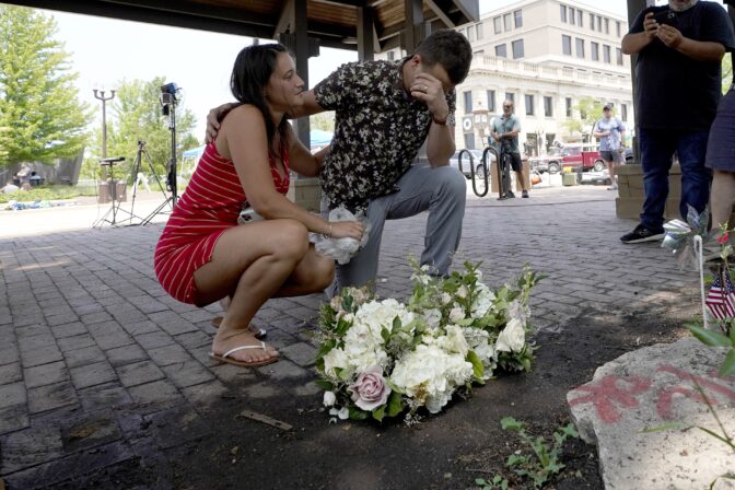 Brooke and Matt Strauss, who were married Sunday, pause after leaving their wedding bouquets in downtown Highland Park, Ill., near the scene of Monday's mass shooting Tuesday, July 5, 2022, in Highland Park, Ill.