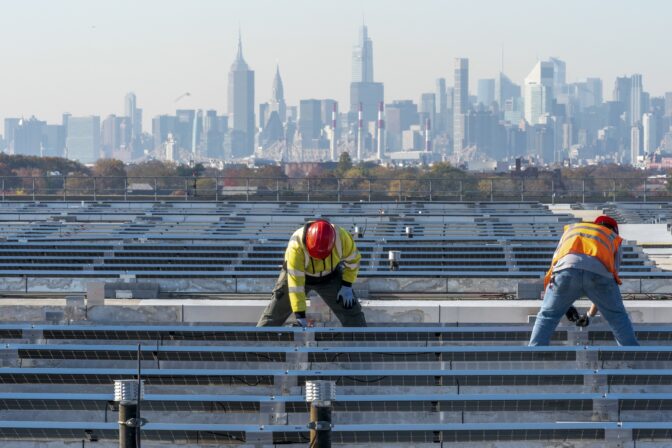 Framed by the Manhattan skyline, electricians with IBEW Local 3 install solar panels on top of the Terminal B garage at LaGuardia Airport, Nov. 9, 2021, in the Queens borough of New York.