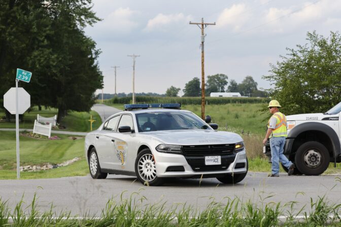 A Clinton County employee helps direct traffic as an Ohio State Highway Patrol vehicle leaves the scene where an armed man was shot and killed by police after breaching the FBI's Cincinnati field office Thursday, Aug. 11, 2022, in Wilmington, Ohio.